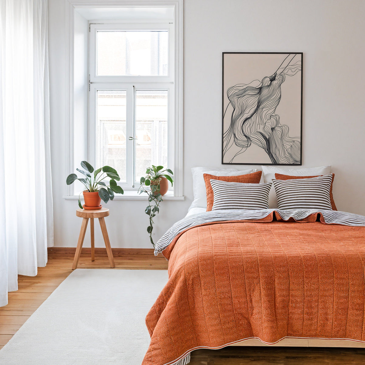 Fine line flowing contour line art print in a thin black frame above a bed with a rust orange quilt