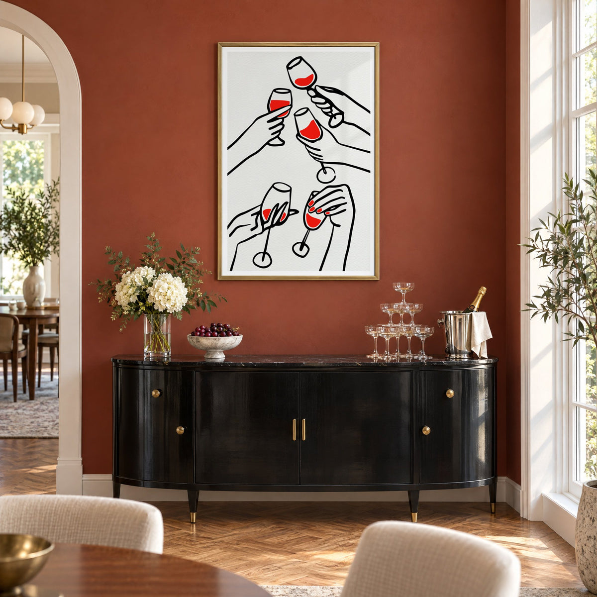 Five hands red wine toast line print in a brass frame on a terracotta wall above a black buffet with a champagne tower