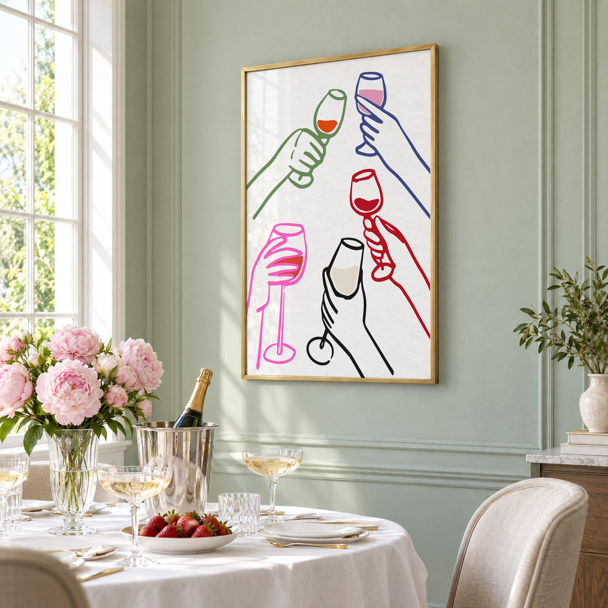 Five hands multicolor wine toast print in a brass frame on a sage wall above a brunch table with champagne and peonies, seen at an angle