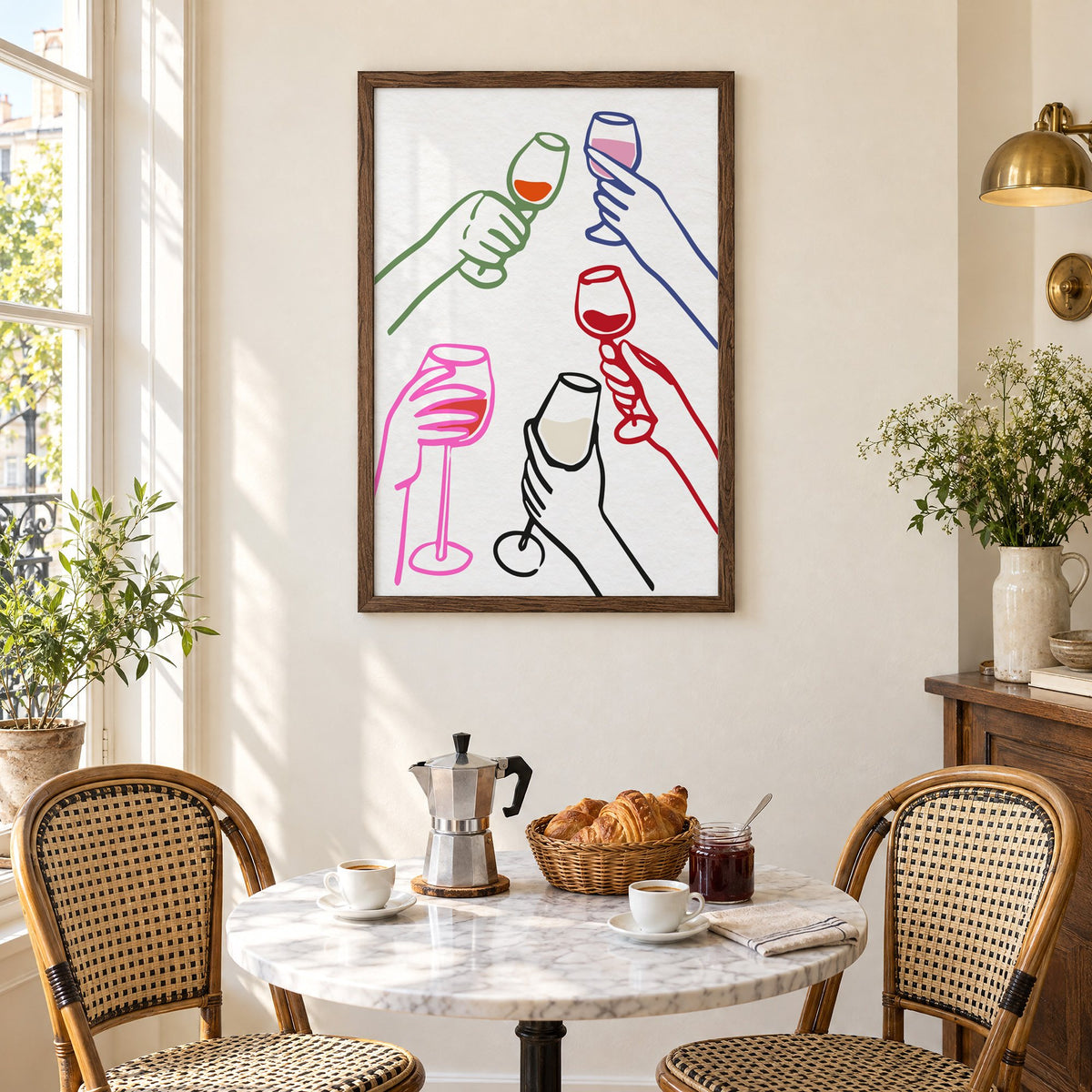 Five hands multicolor wine toast print in a walnut frame above a marble bistro table with croissants and rattan chairs