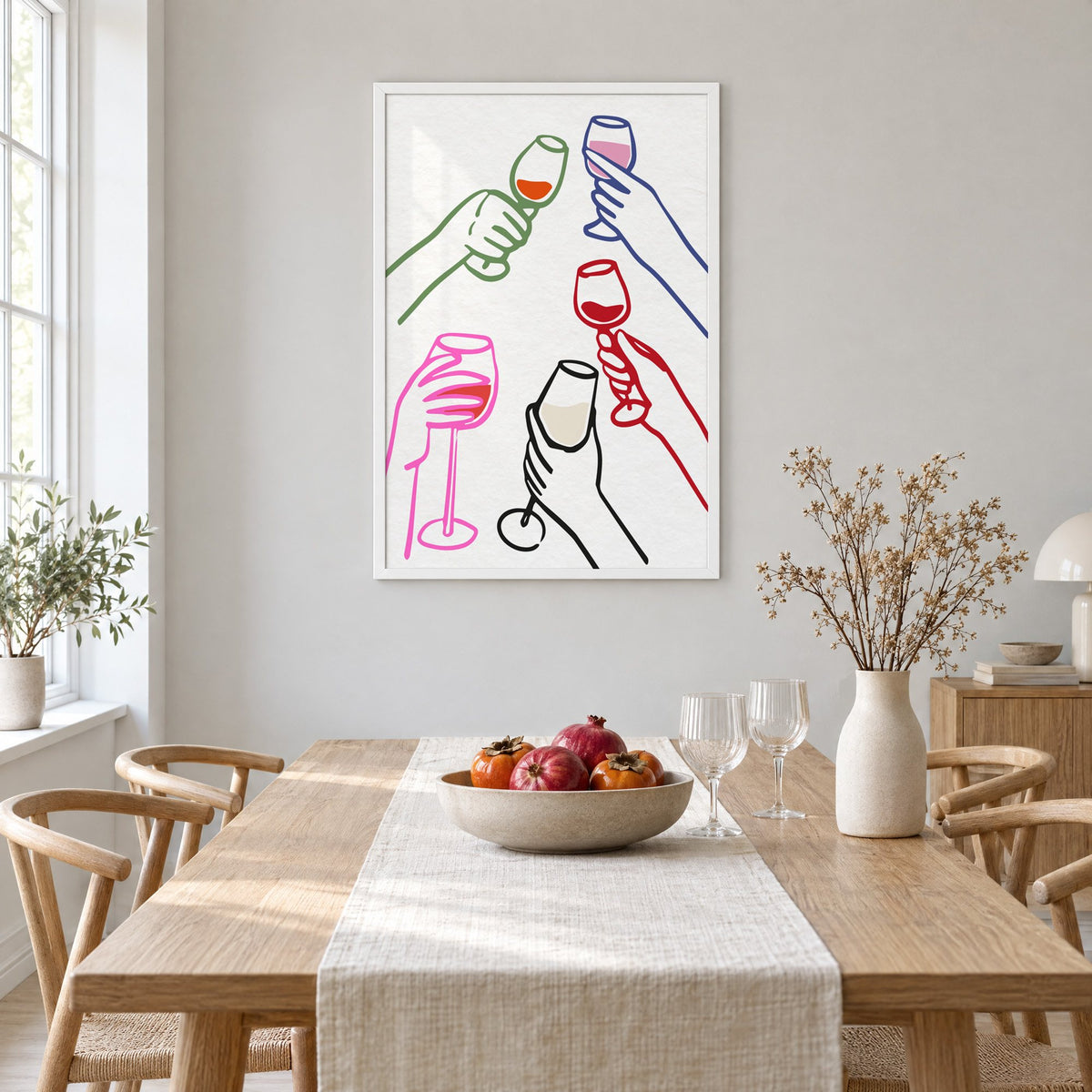 Five hands multicolor wine toast print in a white frame above a light oak dining table with a linen runner and fruit bowl