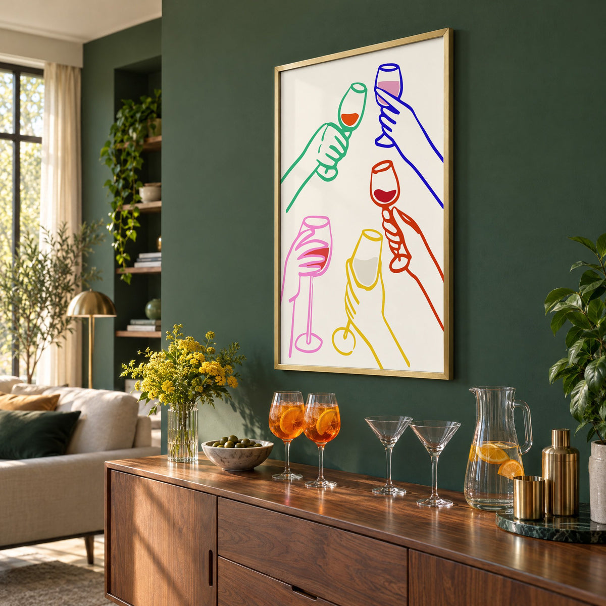 Five hands colorful line wine toast print in a brass frame on a bottle green wall above a sideboard with spritz and martini glasses, seen at an angle