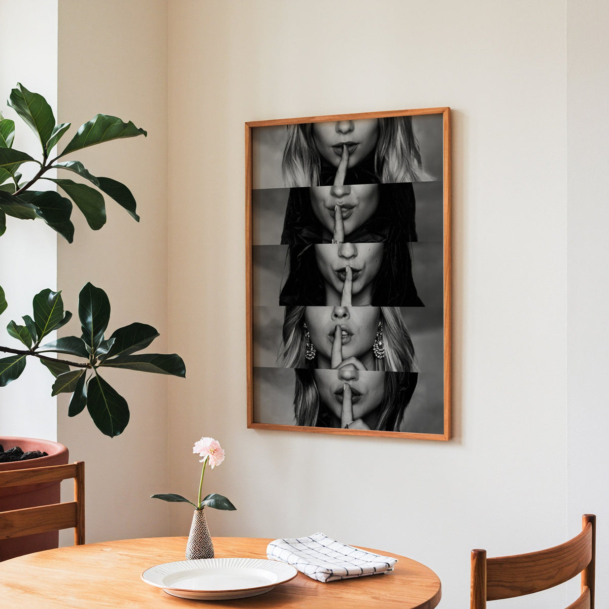 Five stacked strips of finger to lips hush print in a teak frame above a round wooden dining table