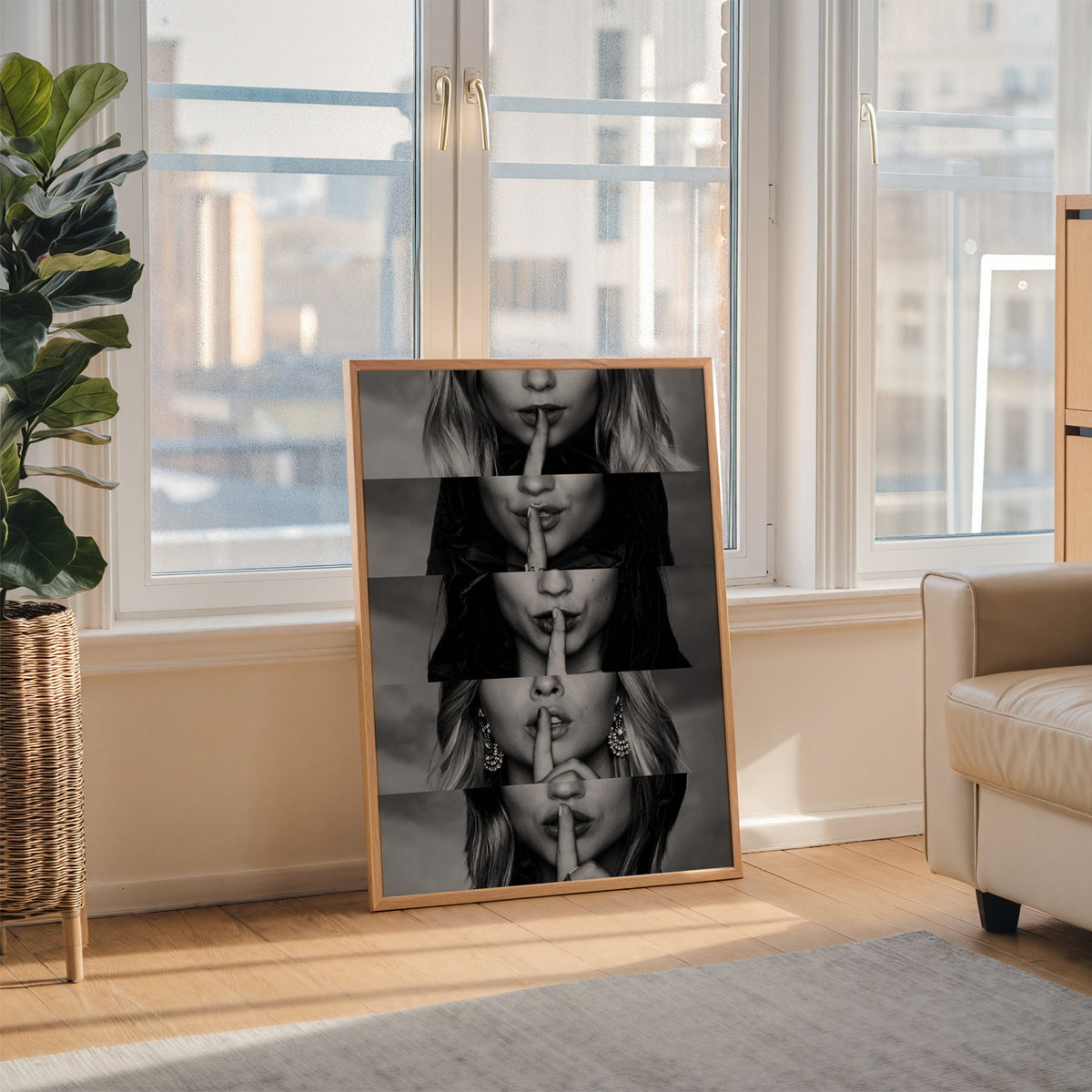 Five stacked strips of finger to lips hush print in an oak frame leaning on the floor beside a fiddle leaf fig