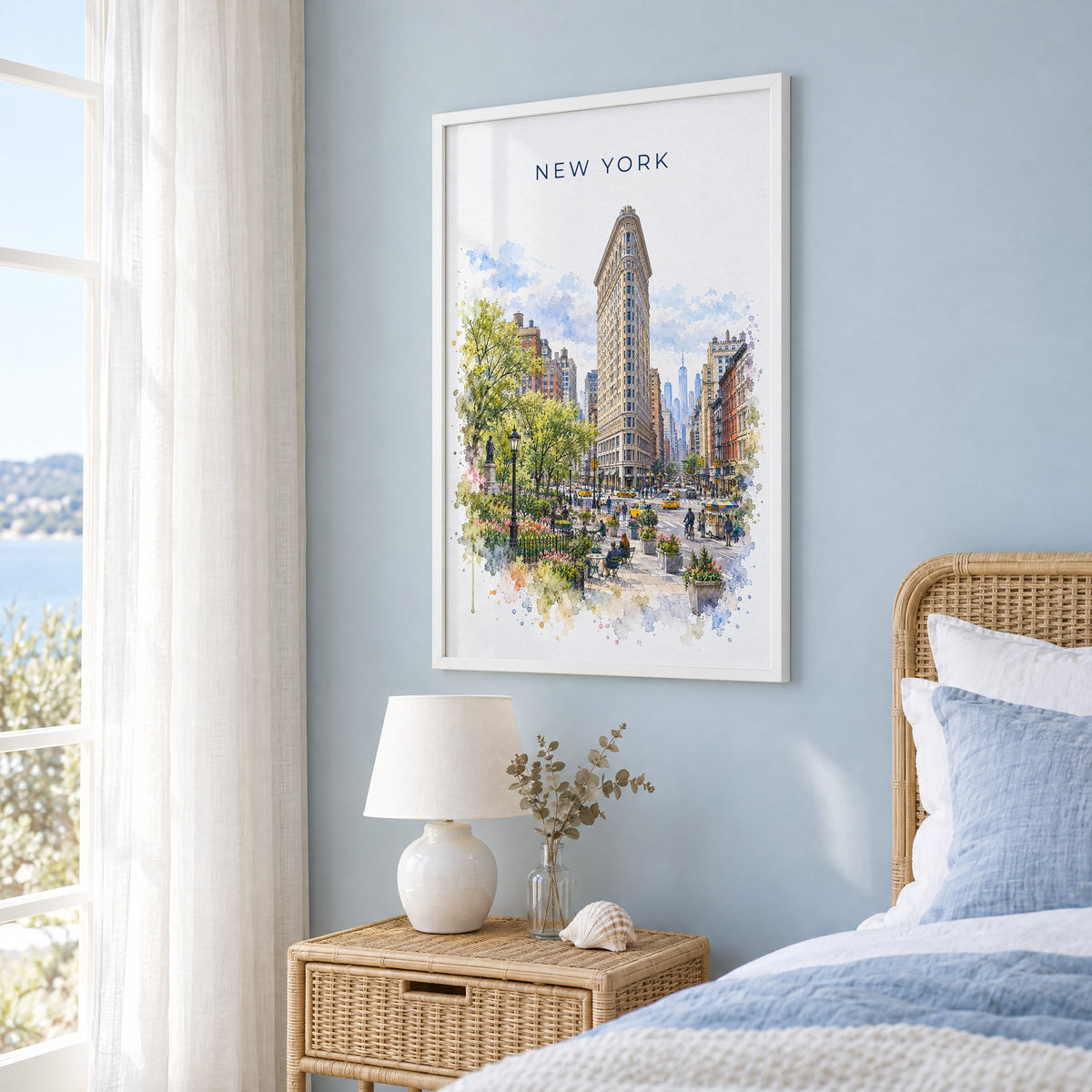 Flatiron Building watercolor print in a white frame on a pale blue wall beside a rattan bed in a coastal bedroom