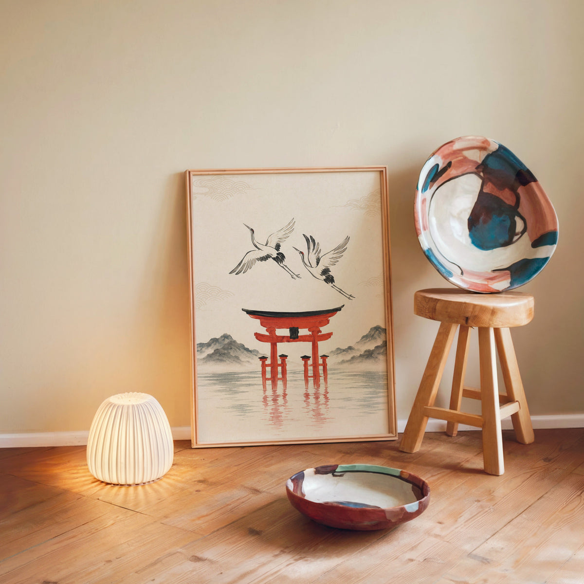 red torii gate with cranes print in a light wood frame leaning on a wooden floor by a glowing lamp and stool