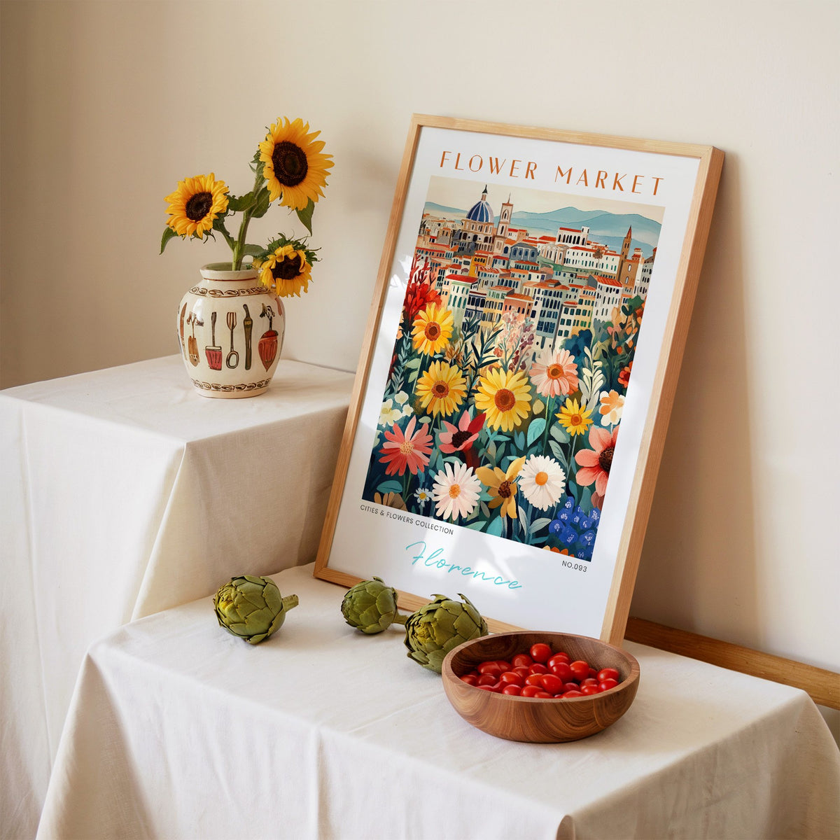 Florence flower market print in an oak frame leaning on a linen-draped table beside a vase of sunflowers