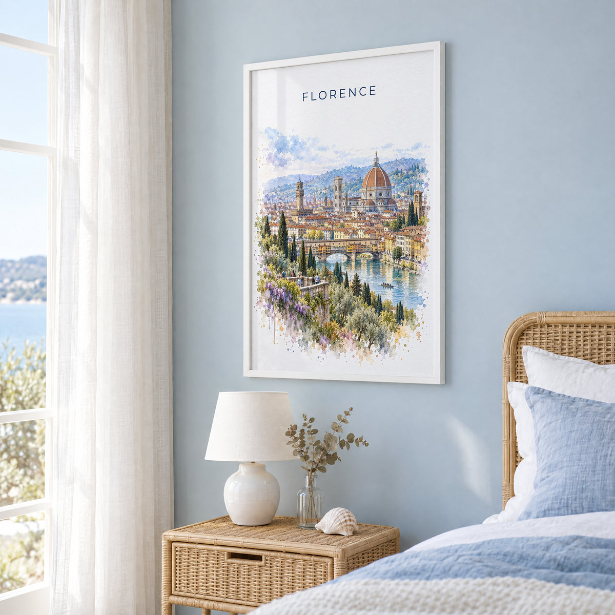 Florence watercolor print in a white frame on a pale blue wall beside a rattan bed in a coastal bedroom