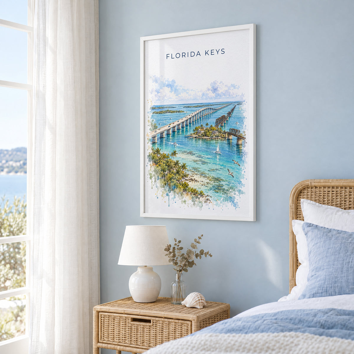Florida Keys watercolor print in a white frame on a pale blue wall beside a rattan bed in a coastal bedroom