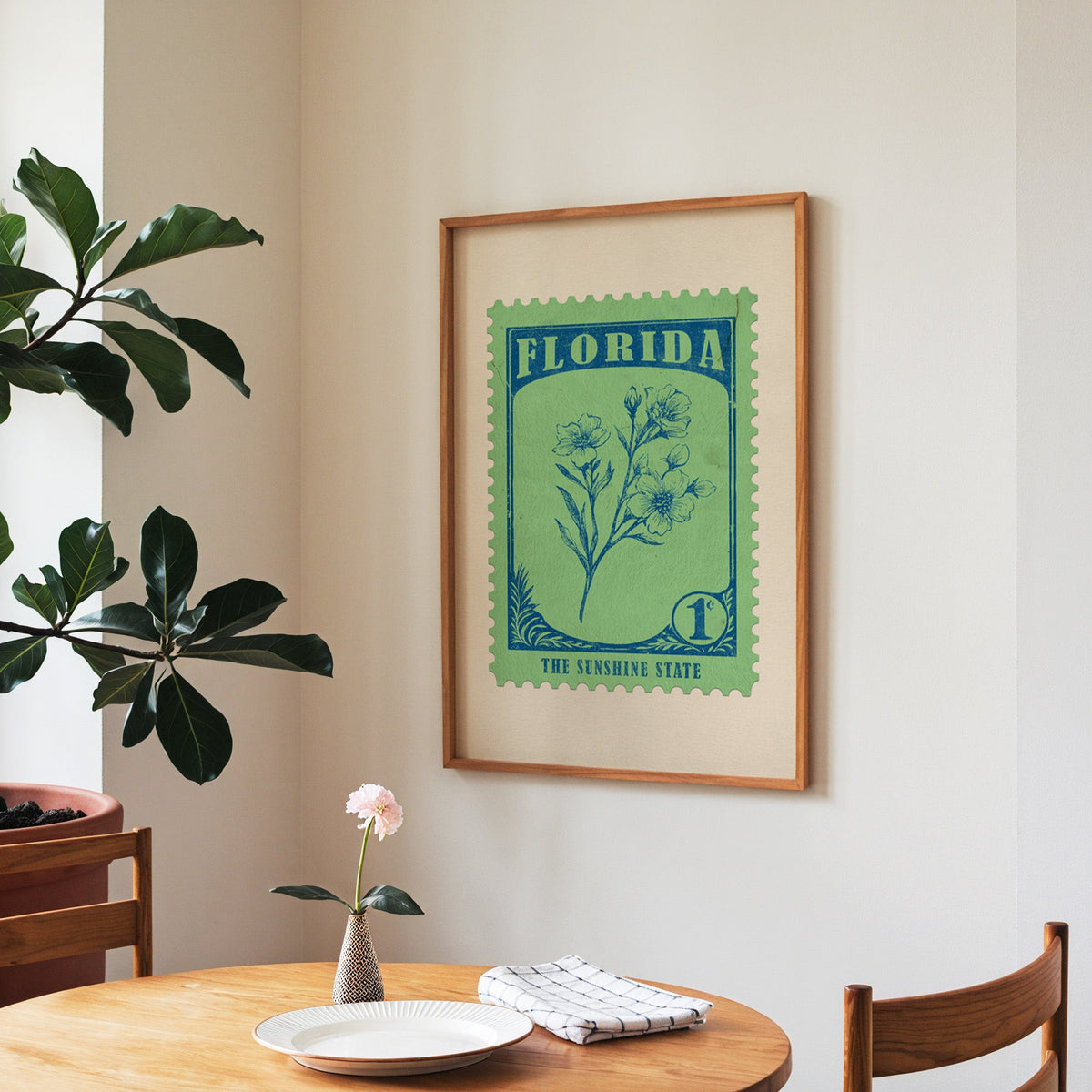 Florida state flower print framed above a round wooden table with a single bloom in a vase and books