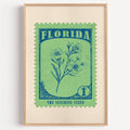Florida state flower stamp print in petrol blue on spring green, light oak frame on a plain white wall