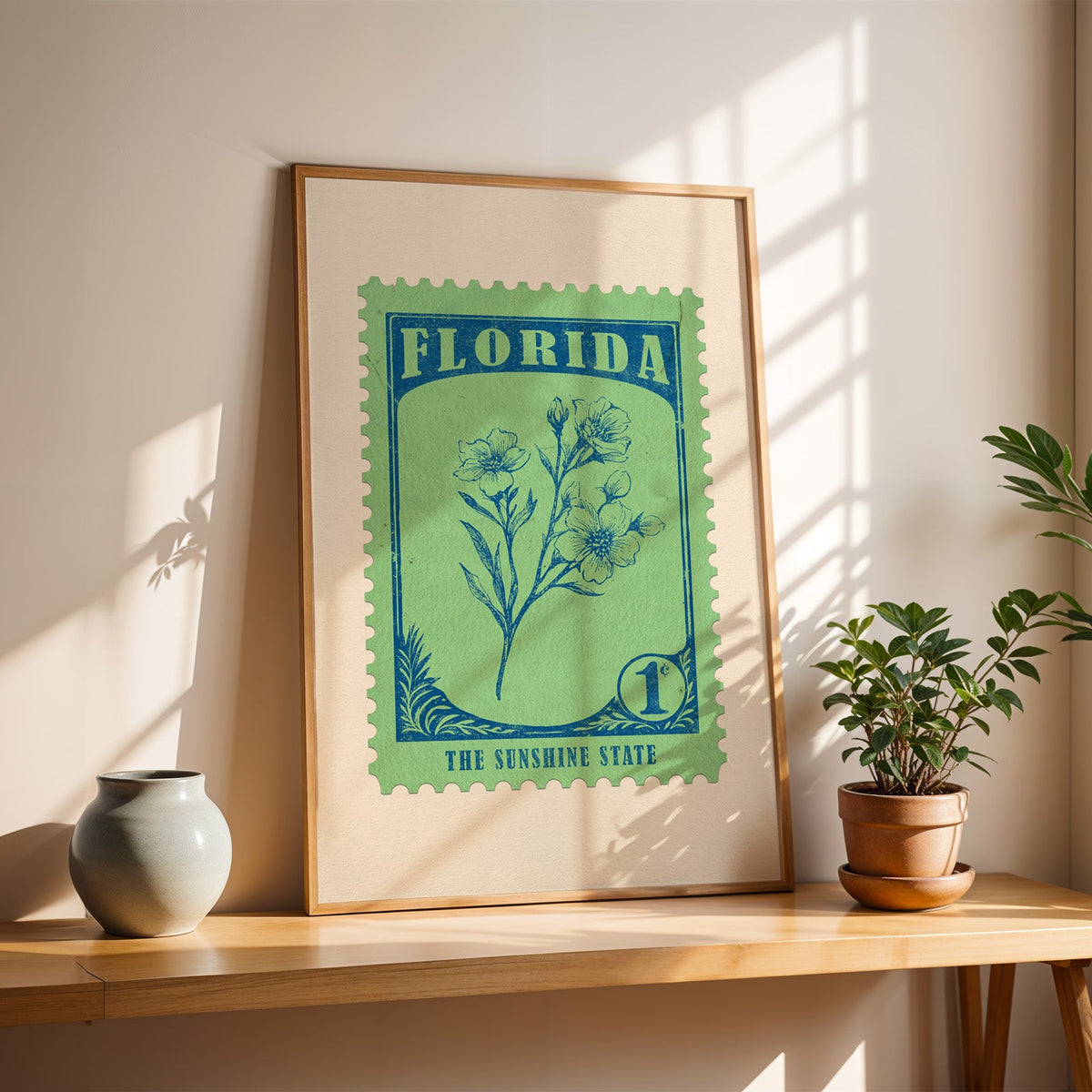 Florida orange blossom stamp print in a light oak frame leaning on a wooden table beside a stoneware vase
