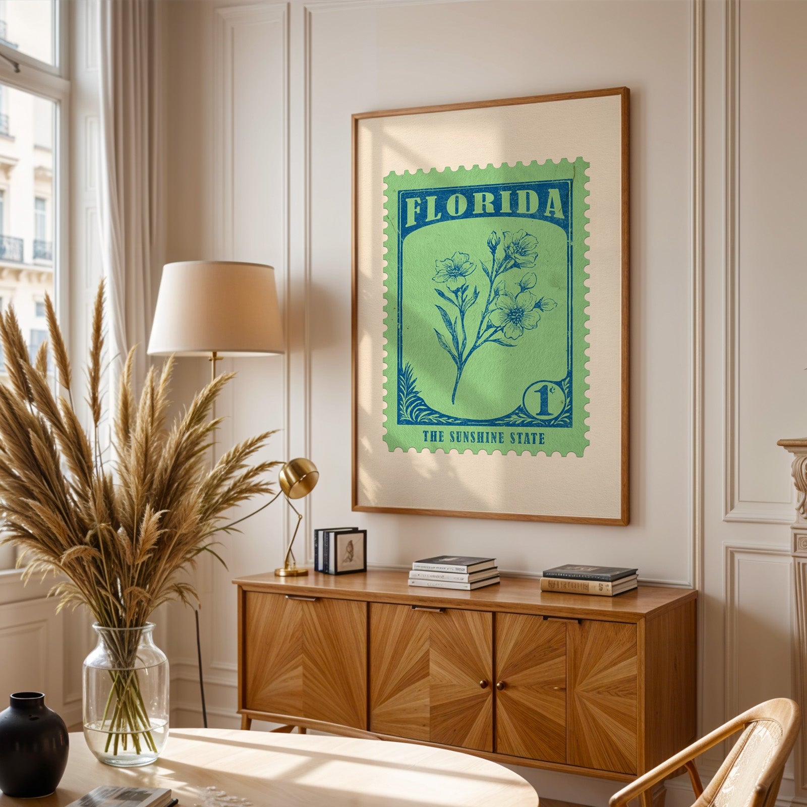 Florida stamp print framed above a wooden sideboard, pampas grass in a glass vase and a floor lamp