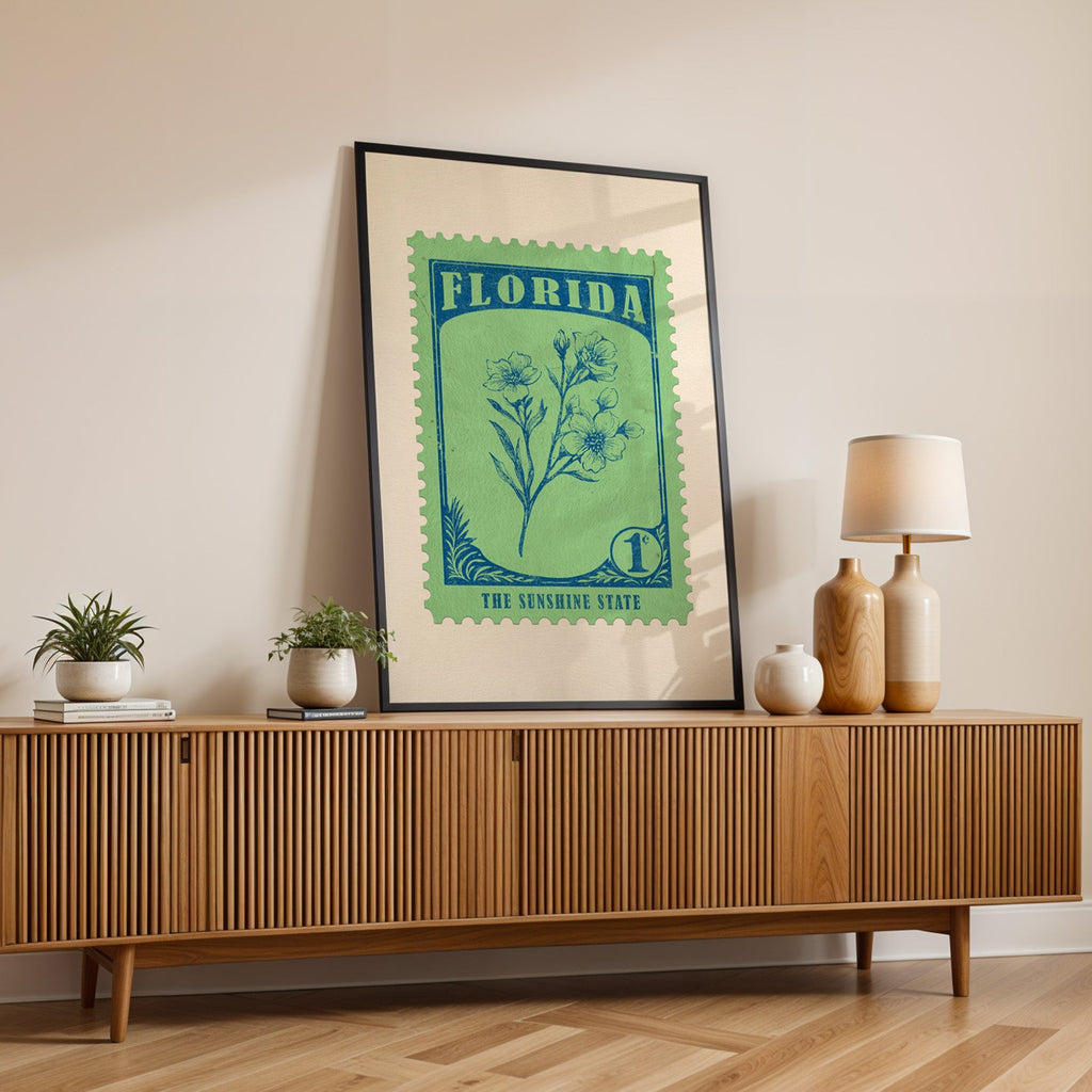 Florida state flower print in a black frame leaning on a fluted wood credenza with vases and a lamp