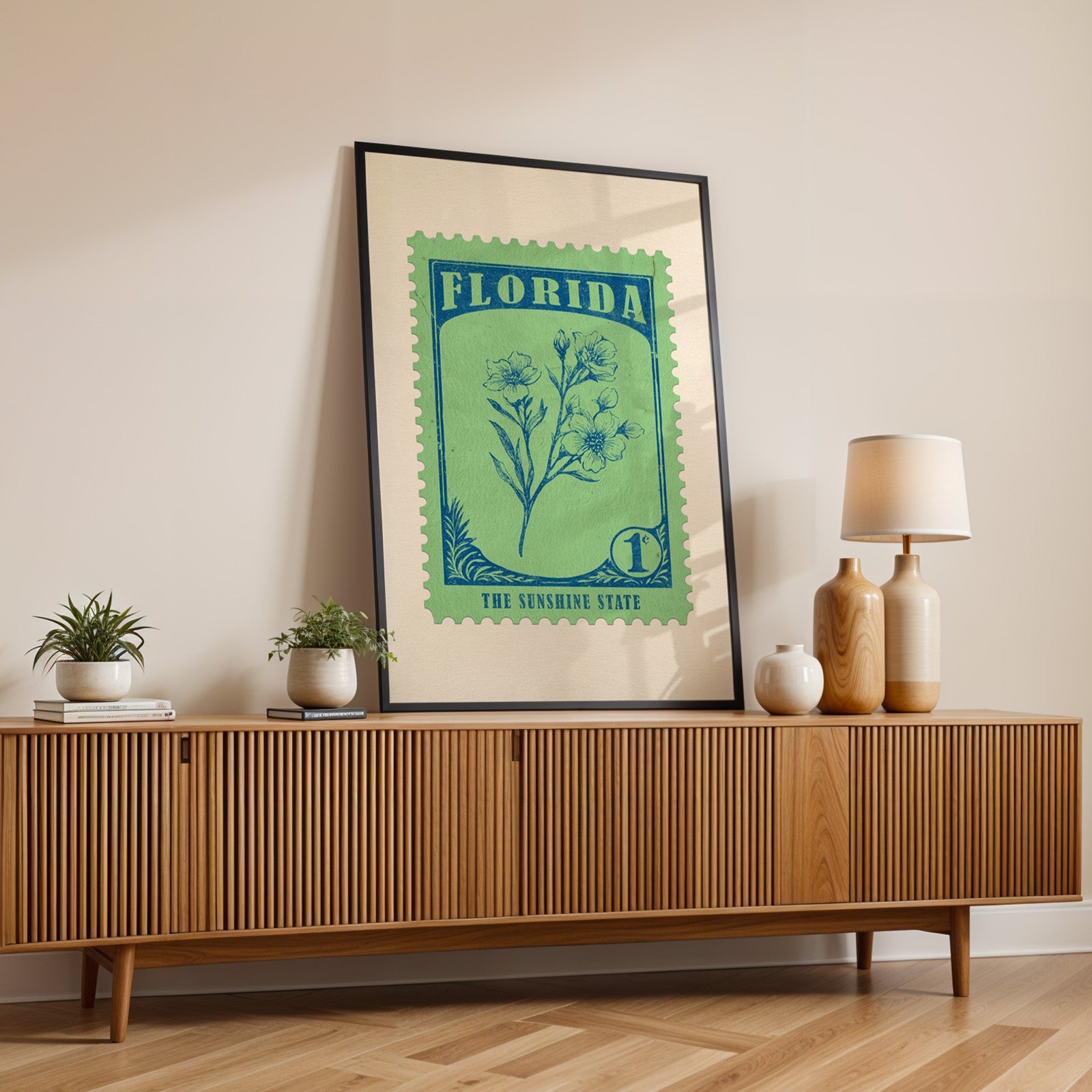 Florida state flower print in a black frame leaning on a fluted wood credenza with vases and a lamp