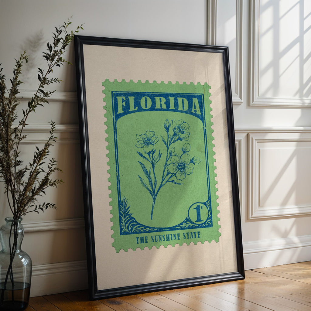 Florida state flower print in a black frame leaning against a white panelled wall beside olive branches