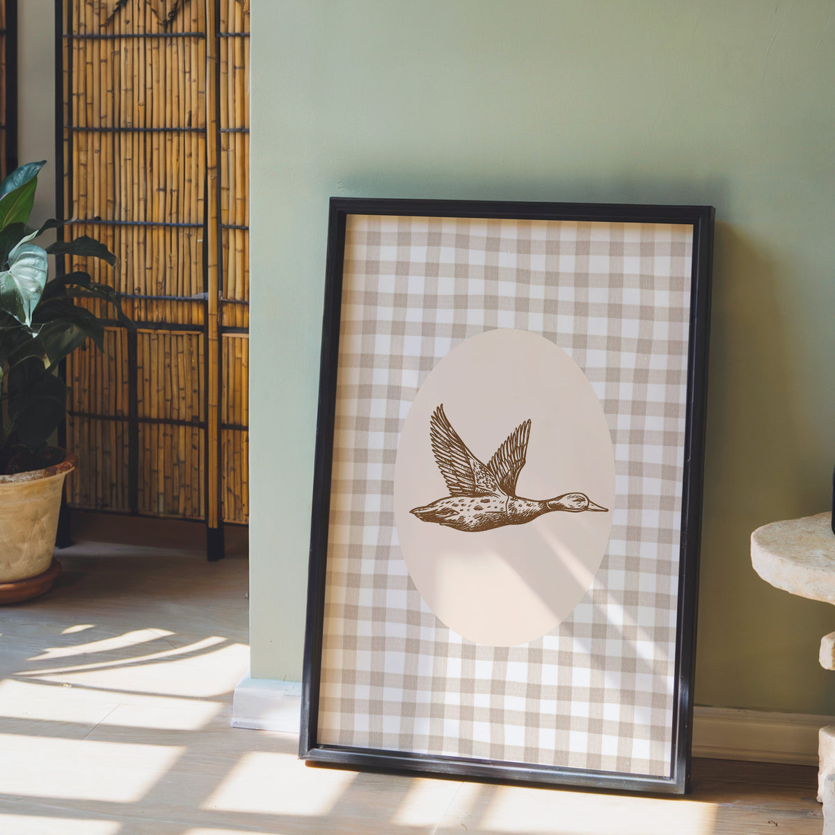 Flying mallard print in a black frame leaning against a sage green wall