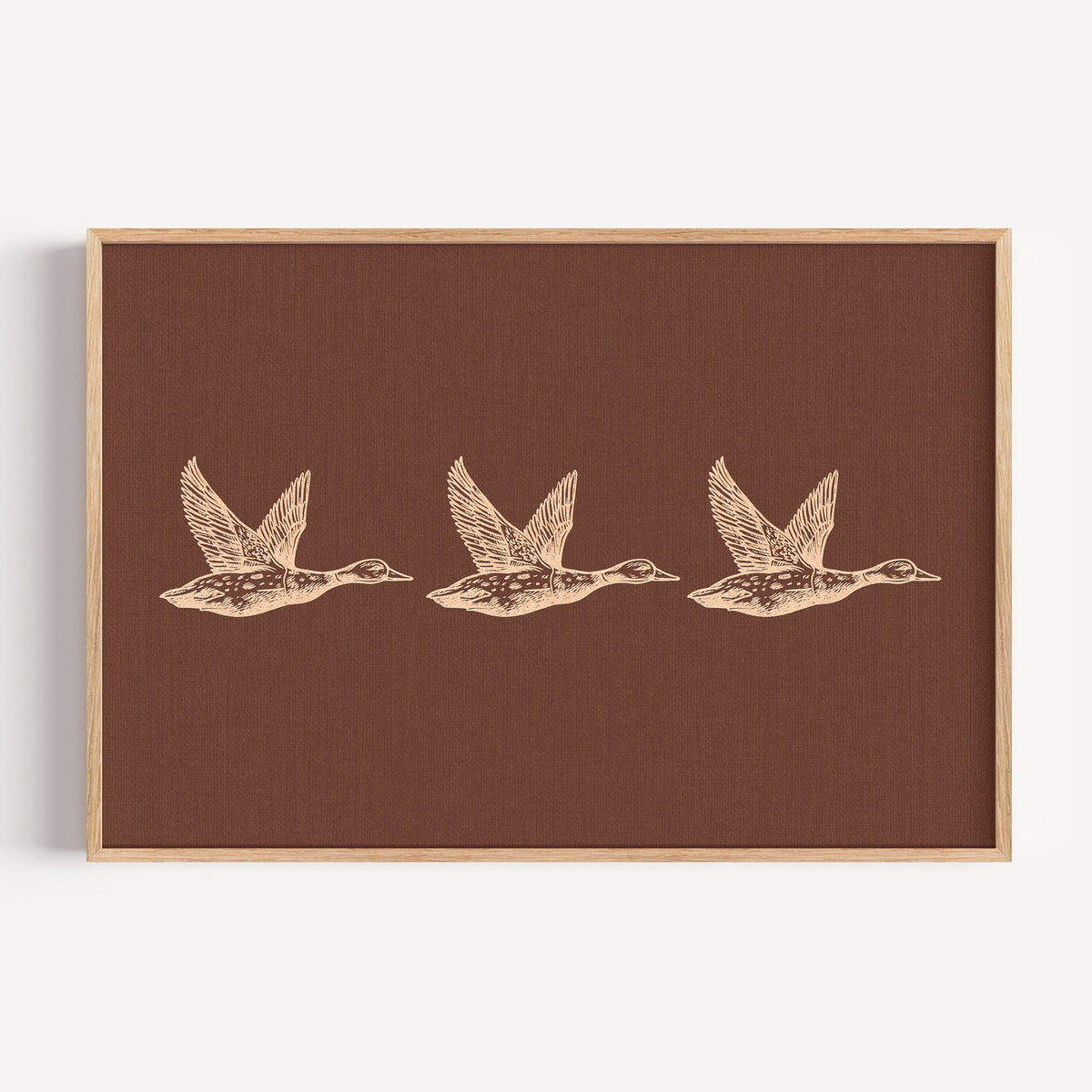 Flying ducks trio print on rust in a light oak frame on a plain white wall