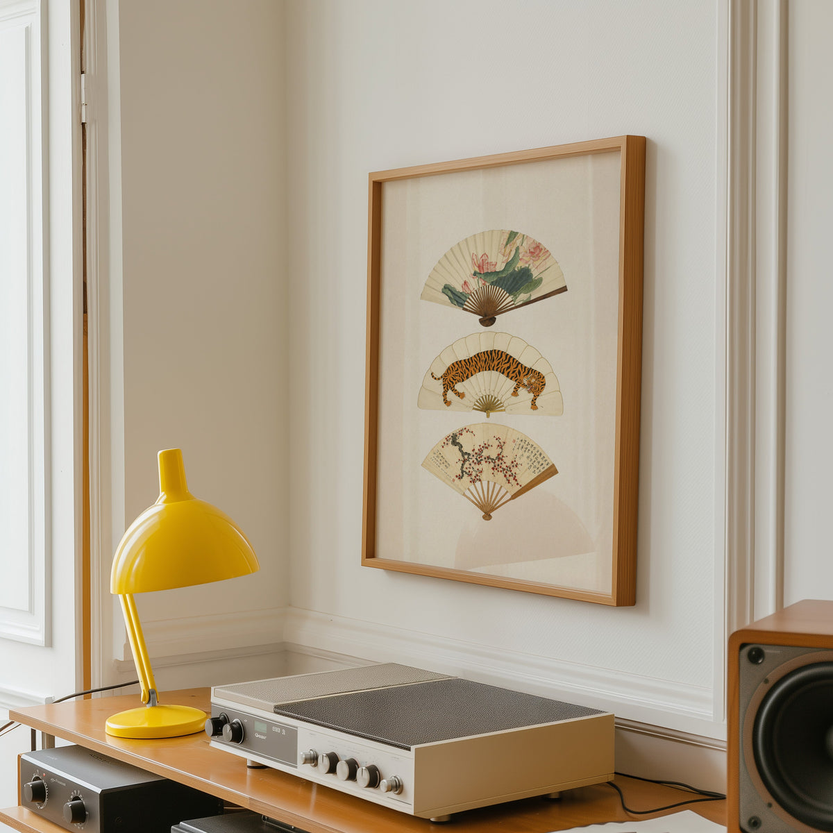 three painted hand fans print in an oak frame above a vintage hi-fi shelf with a yellow desk lamp