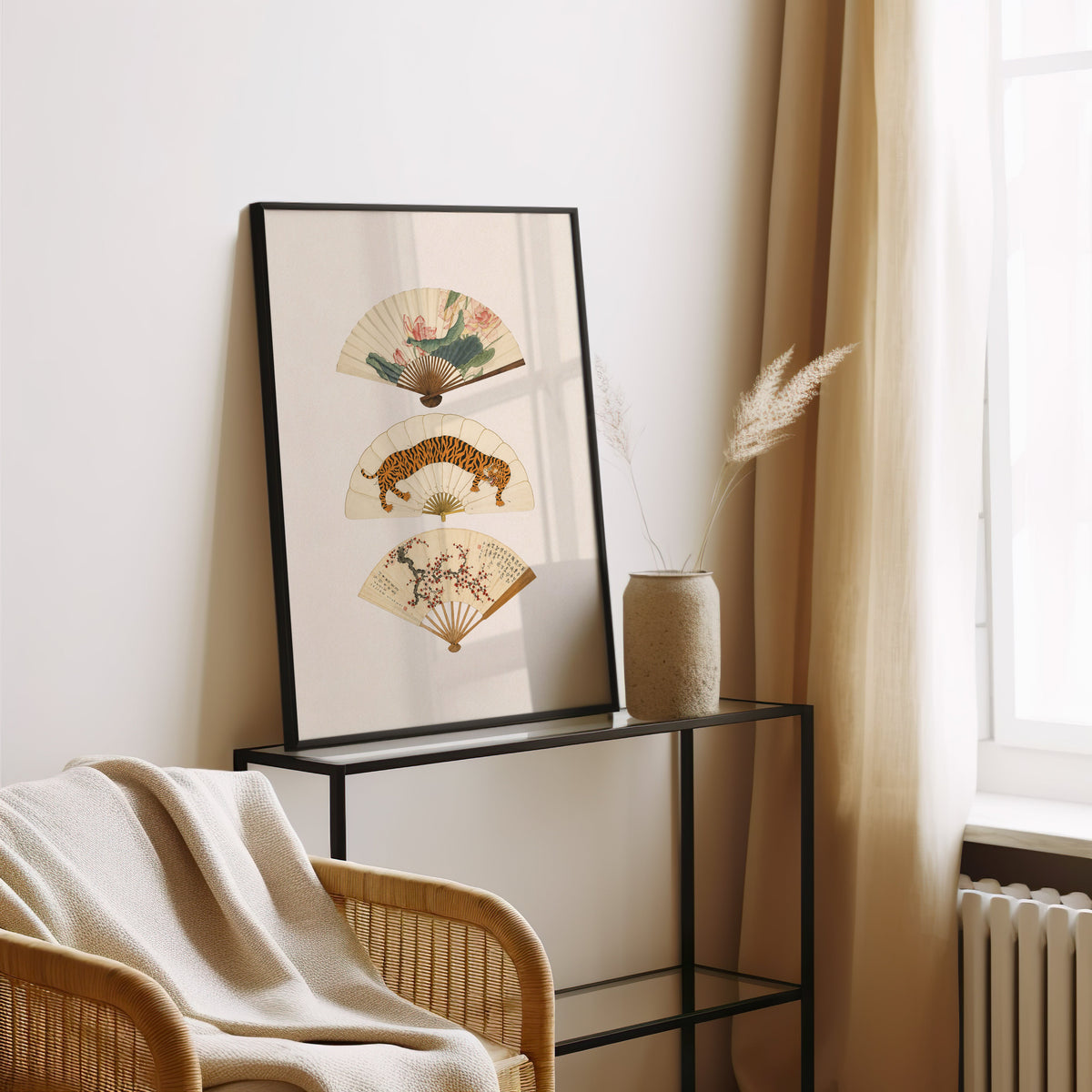 three painted hand fans print in a black frame leaning on a glass console beside pampas grass
