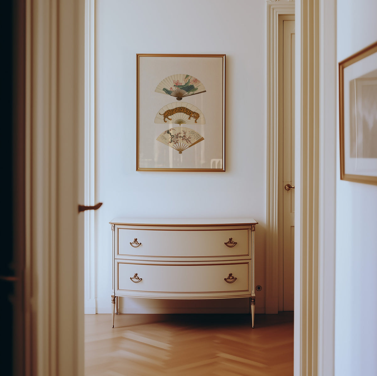 three painted hand fans print shown in a gold frame in a hallway above a cream dresser
