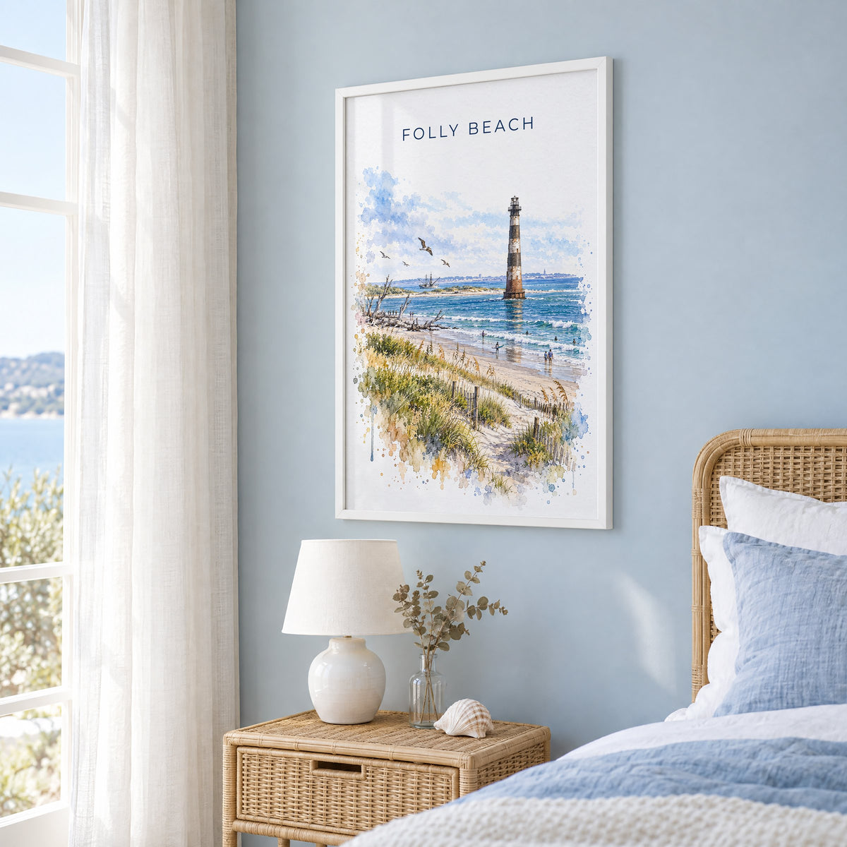 Folly Beach watercolor print in a white frame on a pale blue wall beside a rattan bed in a coastal bedroom