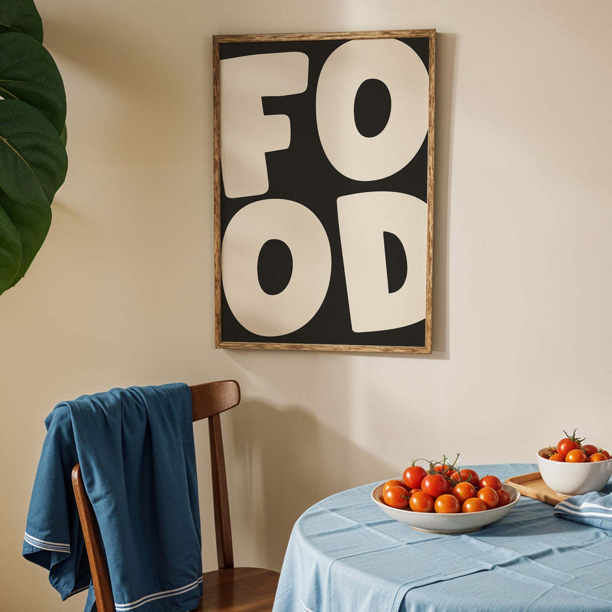 Bold food typography print in an oak frame above a blue linen table with ripe tomatoes