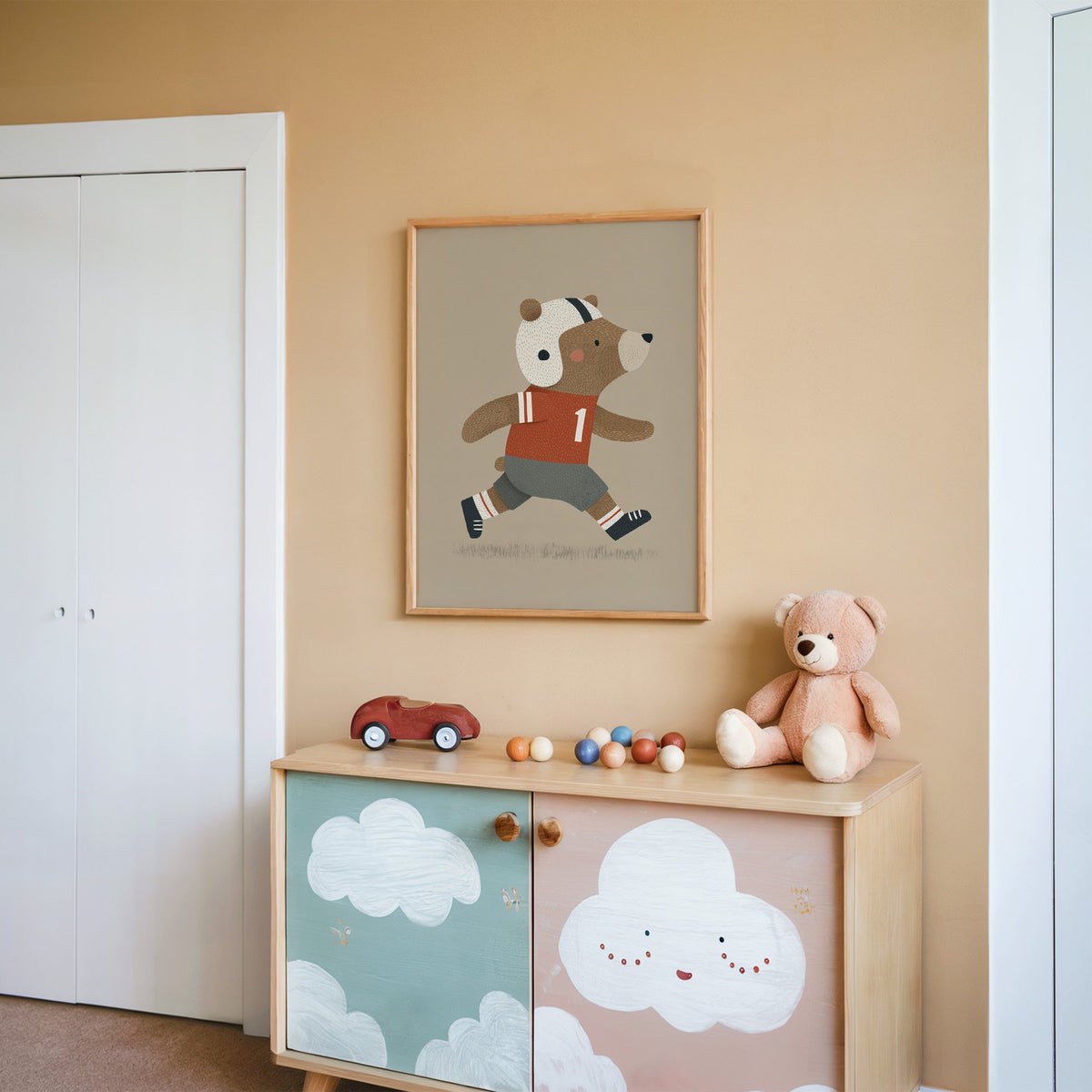 Football bear number one nursery print in an oak frame on a peach wall above a cloud-painted cabinet
