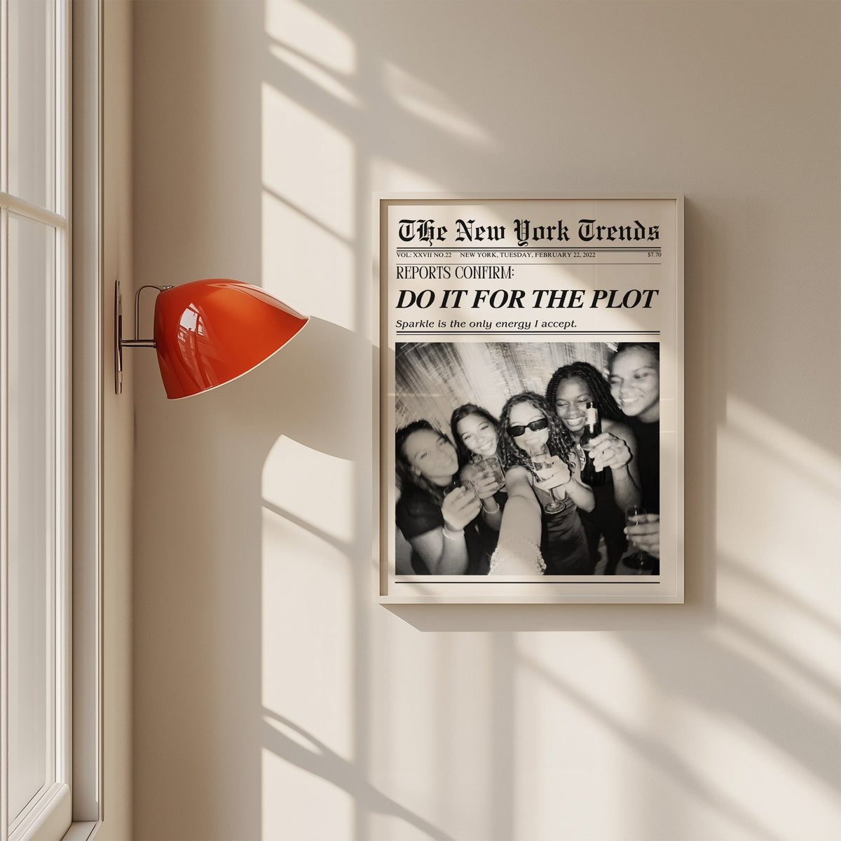 Five friends party selfie mock newspaper print in a white frame on a sunlit wall beside a red sconce