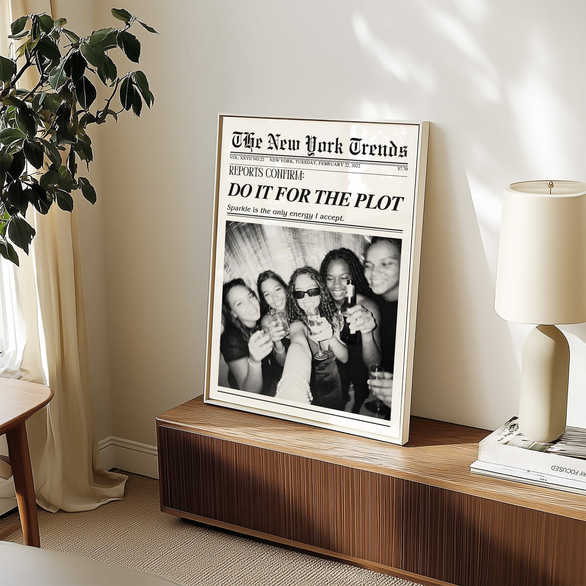 Five friends party selfie mock newspaper print in a white frame on a walnut sideboard beside a ceramic lamp