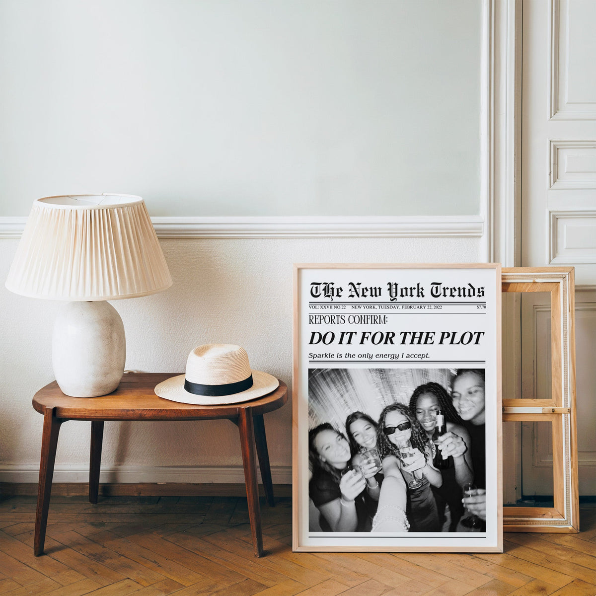 Five friends party selfie mock newspaper print in a pine frame on a wood floor beside a lamp and straw hat