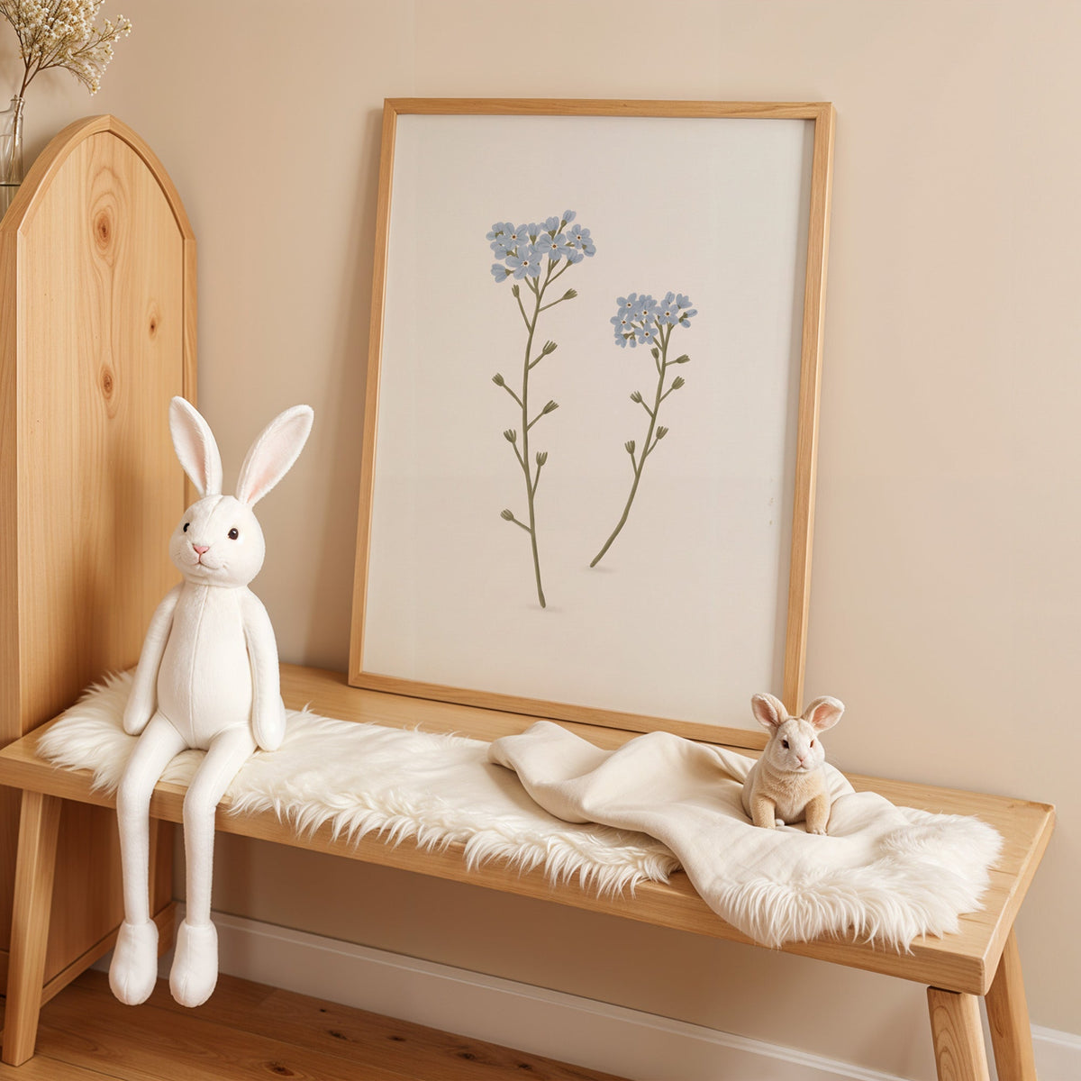 Two blue forget-me-not stems nursery print in an oak frame on a sheepskin bench beside a white plush bunny
