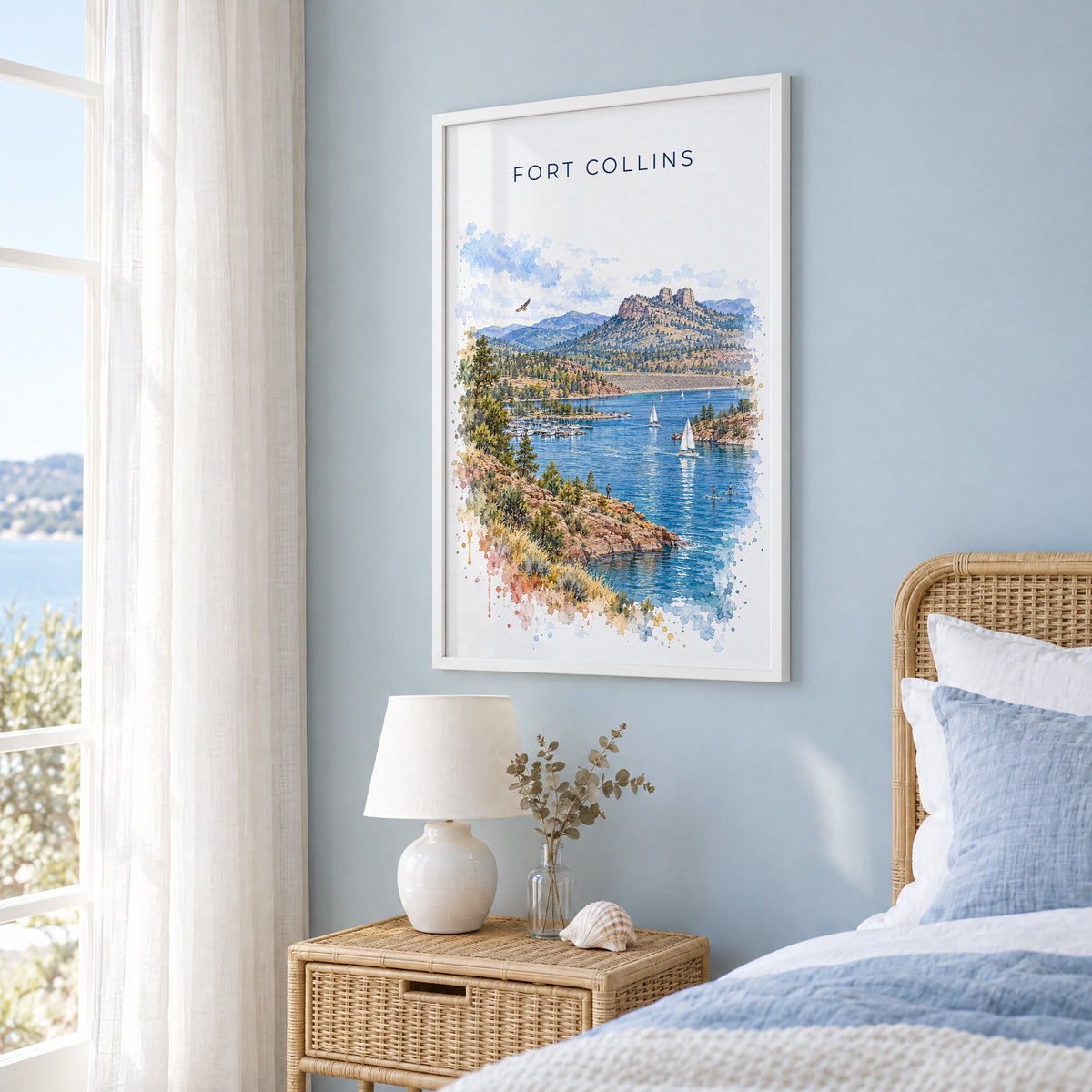 Fort Collins watercolor print in a white frame on a pale blue wall beside a rattan bed in a coastal bedroom