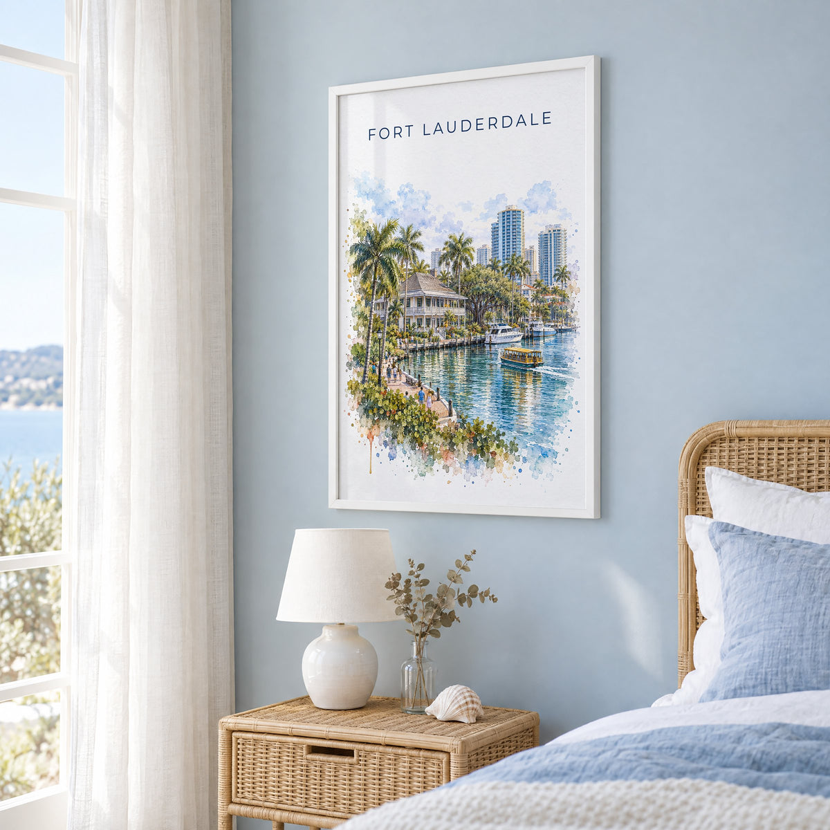 Fort Lauderdale watercolor print in a white frame on a pale blue wall beside a rattan bed in a coastal bedroom