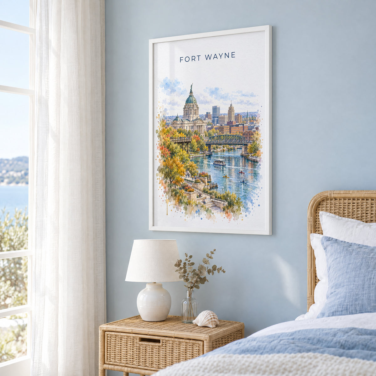 Fort Wayne watercolor print in a white frame on a pale blue wall beside a rattan bed in a coastal bedroom