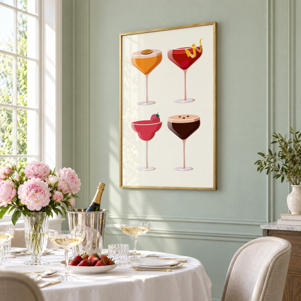 Four coupe cocktails two-by-two grid print in a brass frame on a sage wall above a brunch table with champagne and peonies, seen at an angle