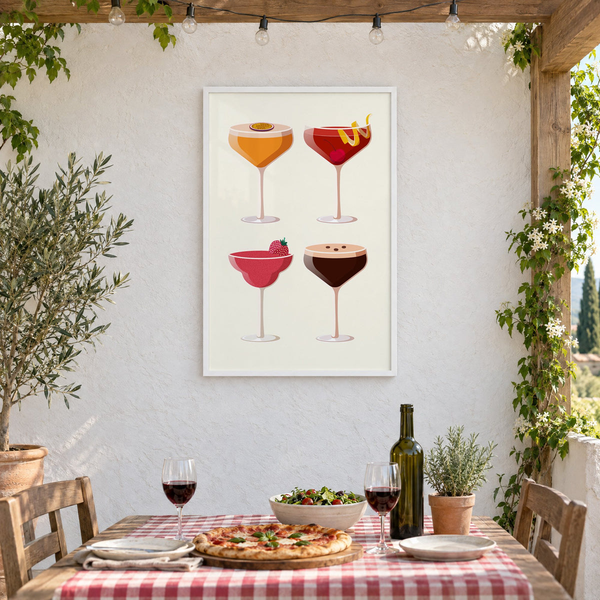 Four coupe cocktails two-by-two grid print in a white frame on a stucco wall above a checked-cloth table with pizza and red wine