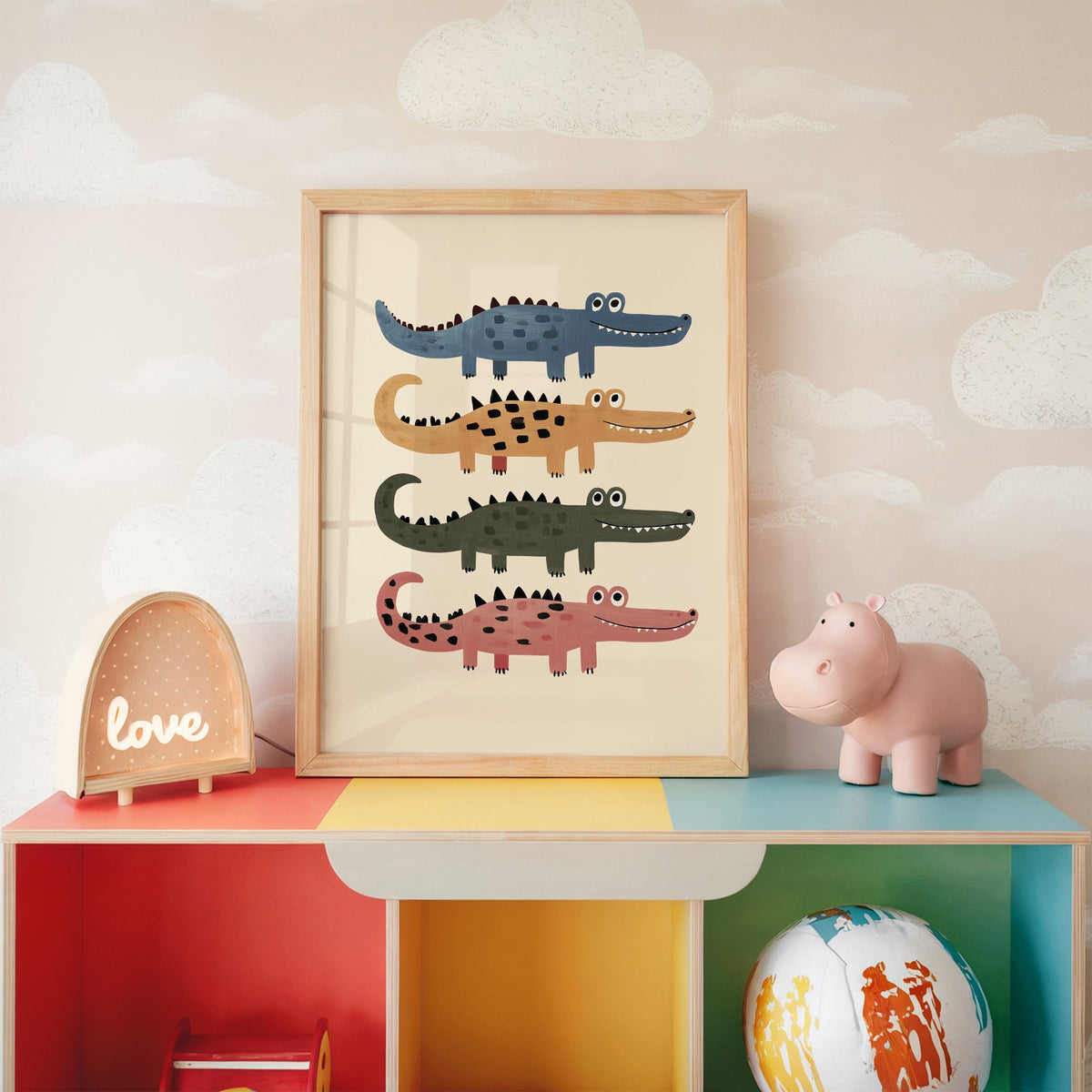 Four stacked crocodiles nursery print in an oak frame on a rainbow toy shelf against cloud wallpaper