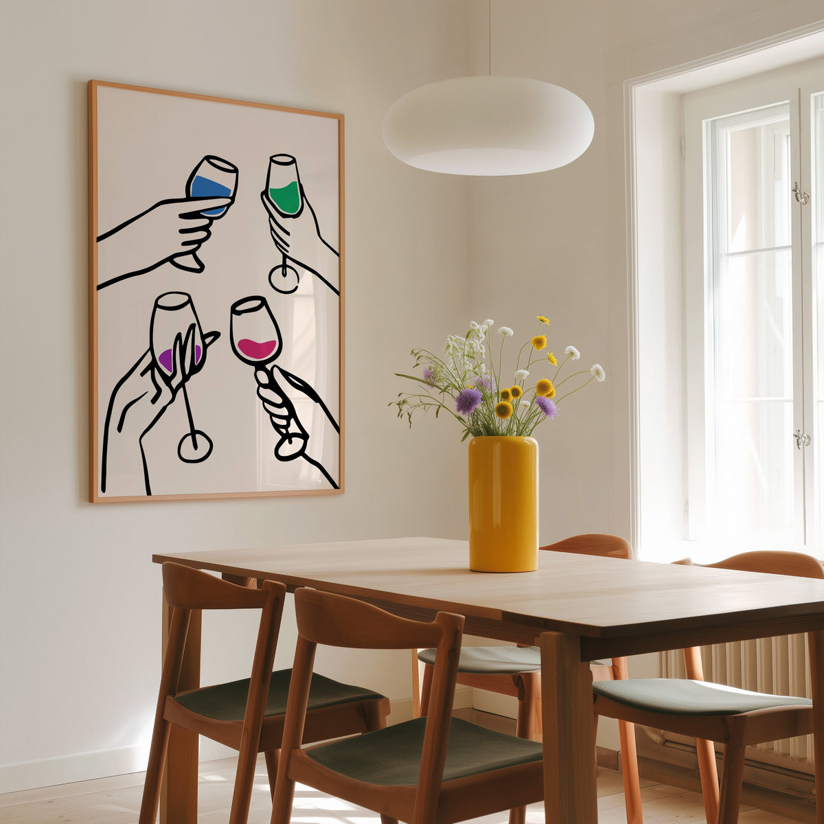 Four hands cheers colour pour print in a slim oak frame above a wooden dining table under a round pendant light