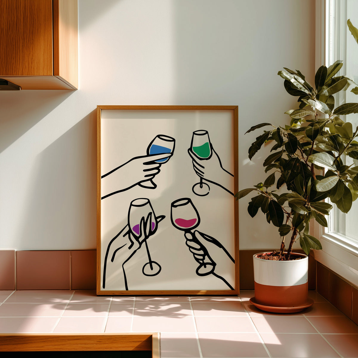 Four hands cheers colour pour print in a golden oak frame leaning on a pink tiled ledge in strong afternoon sun