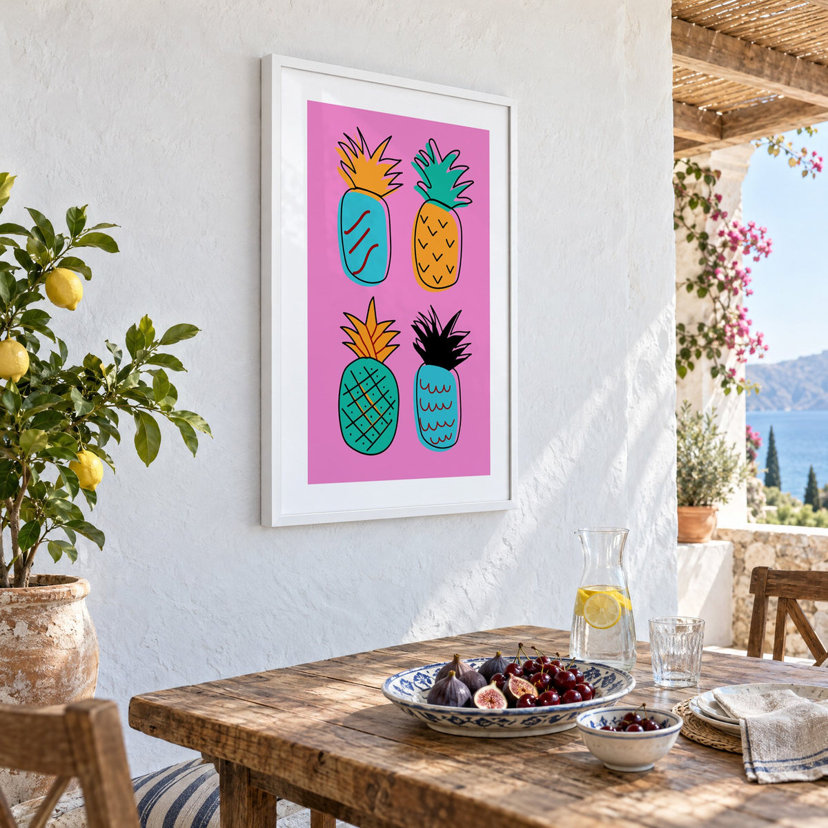 four patterned doodle pineapples hot pink print in a white frame on a whitewashed terrace wall above a lunch table with figs and cherries, seen at an angle