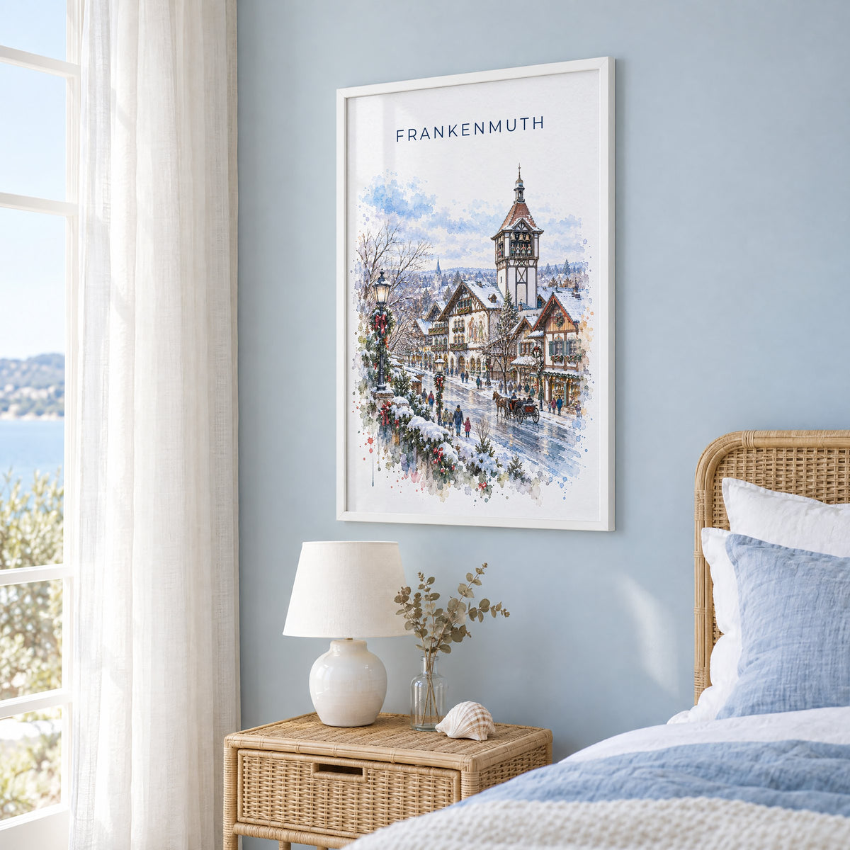 Frankenmuth watercolor print in a white frame on a pale blue wall beside a rattan bed in a coastal bedroom