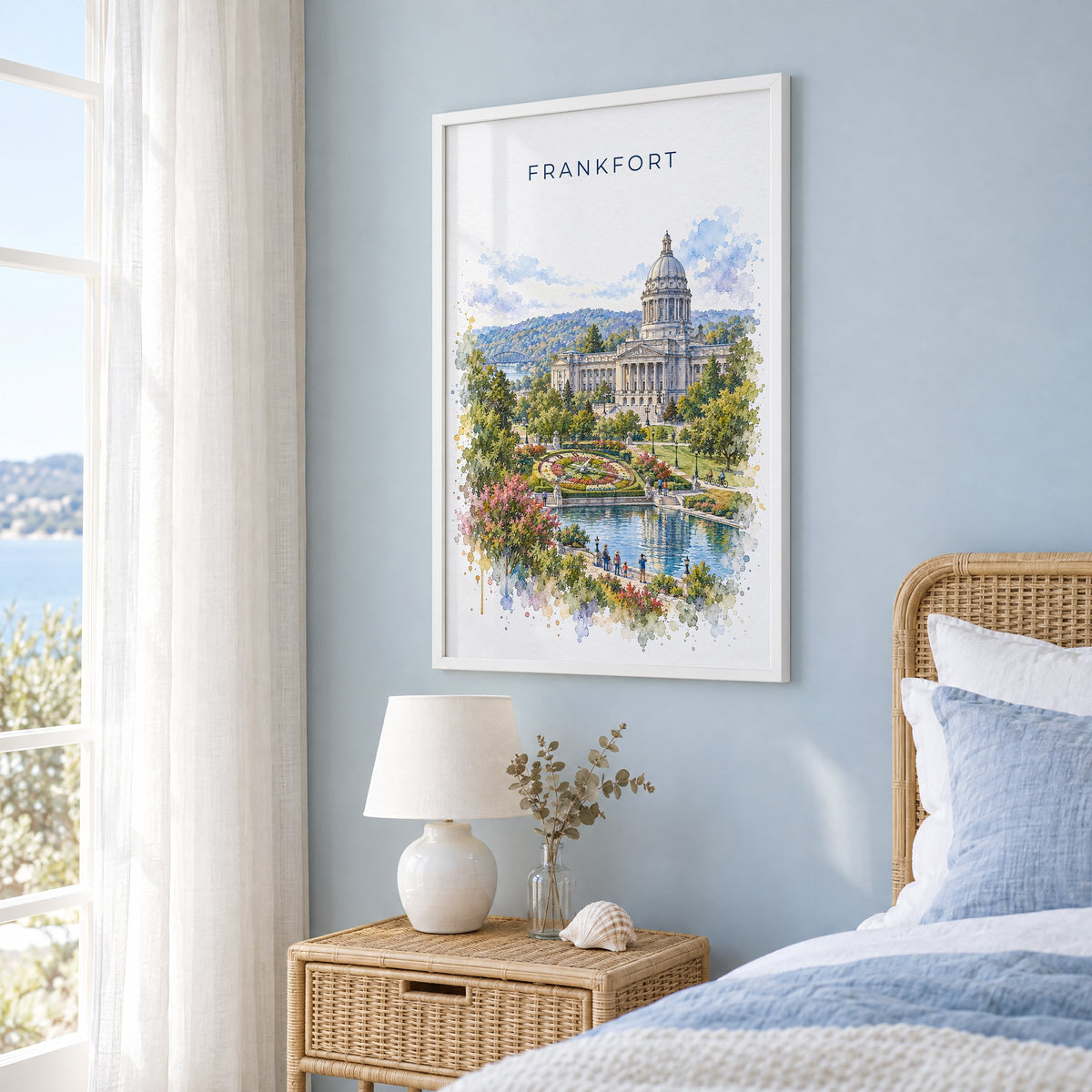 Frankfort, Kentucky watercolor print in a white frame on a pale blue wall beside a rattan bed in a coastal bedroom