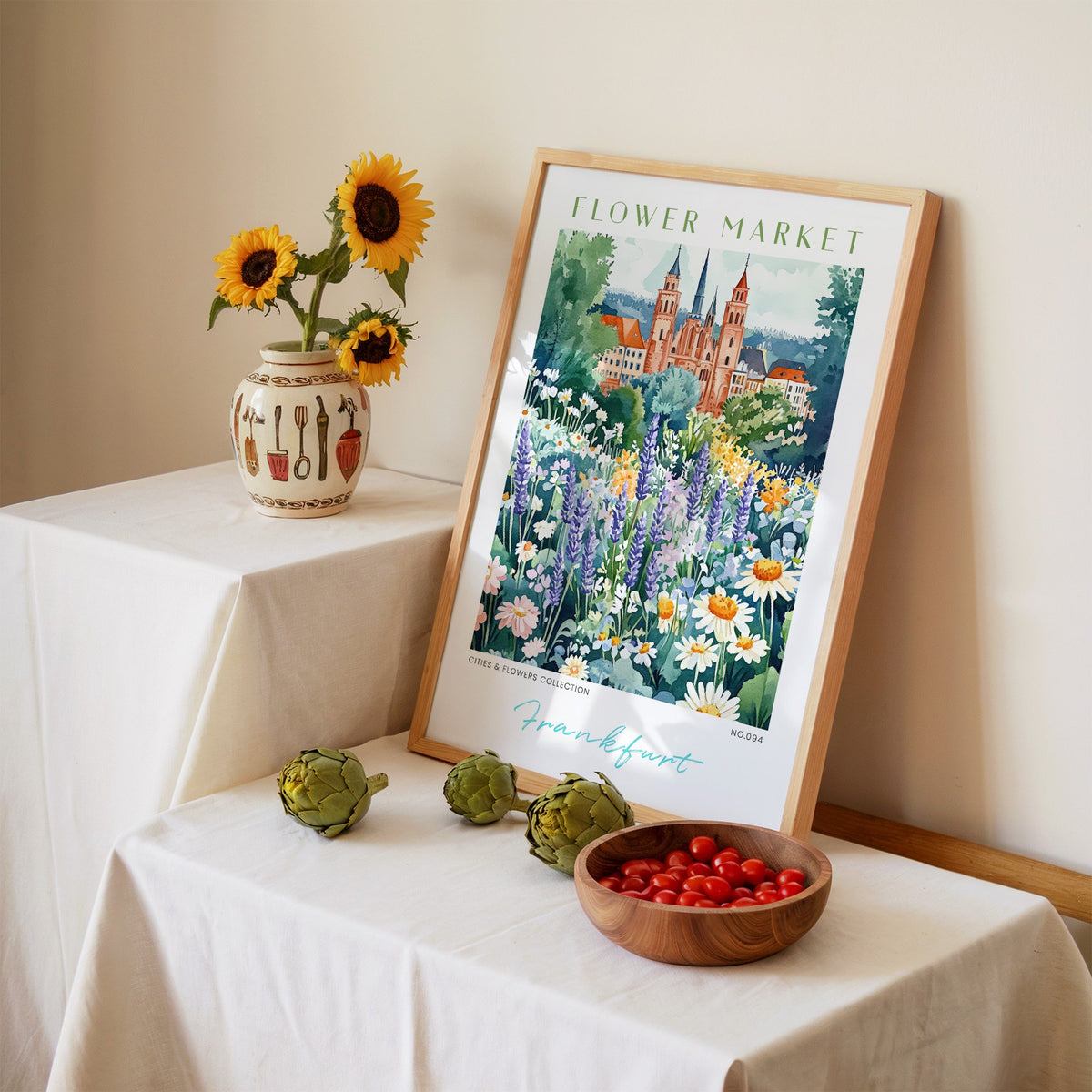 Frankfurt flower market print in an oak frame leaning on a linen-draped table beside a vase of sunflowers