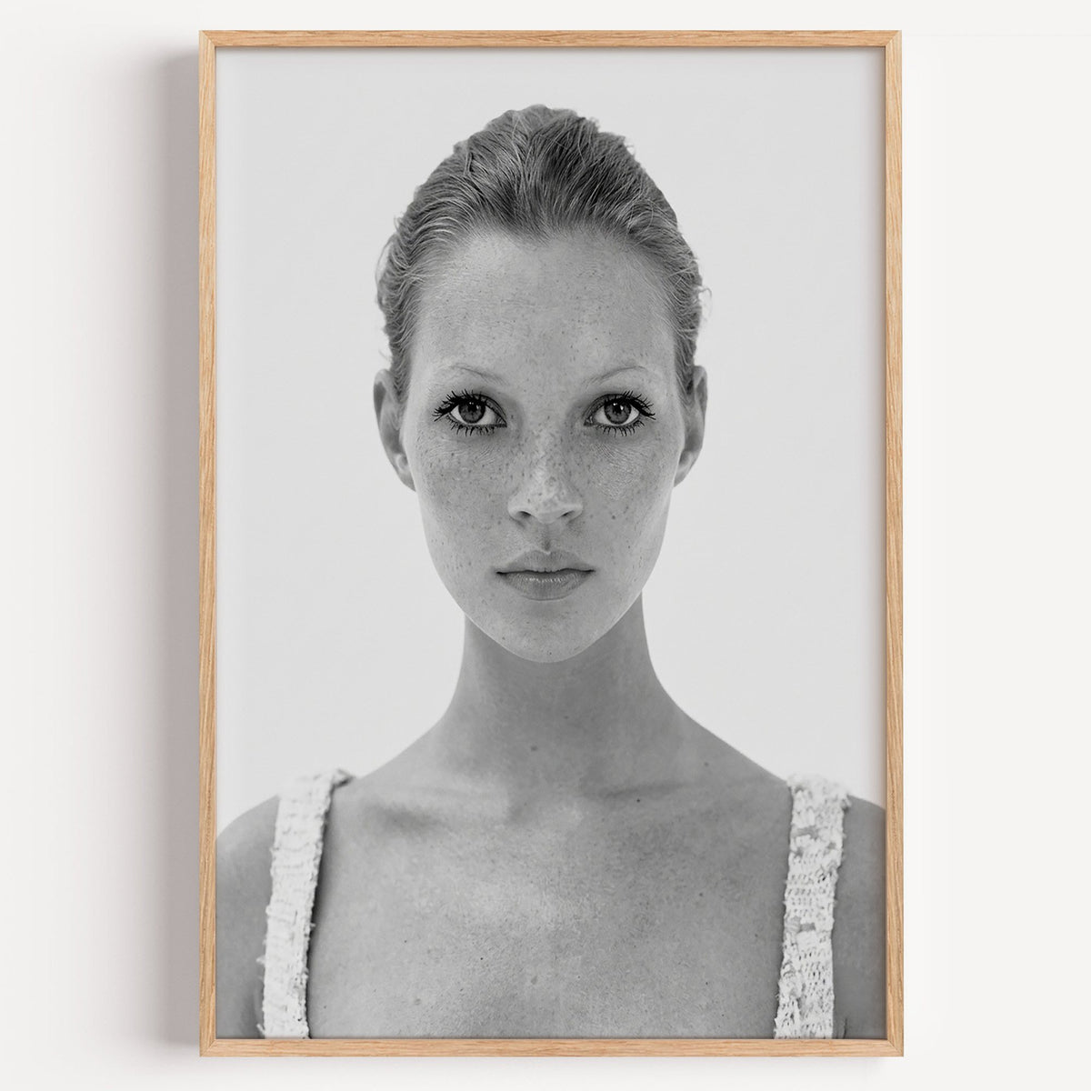 Freckled woman in lace tank top portrait print in a light oak frame on a plain white wall