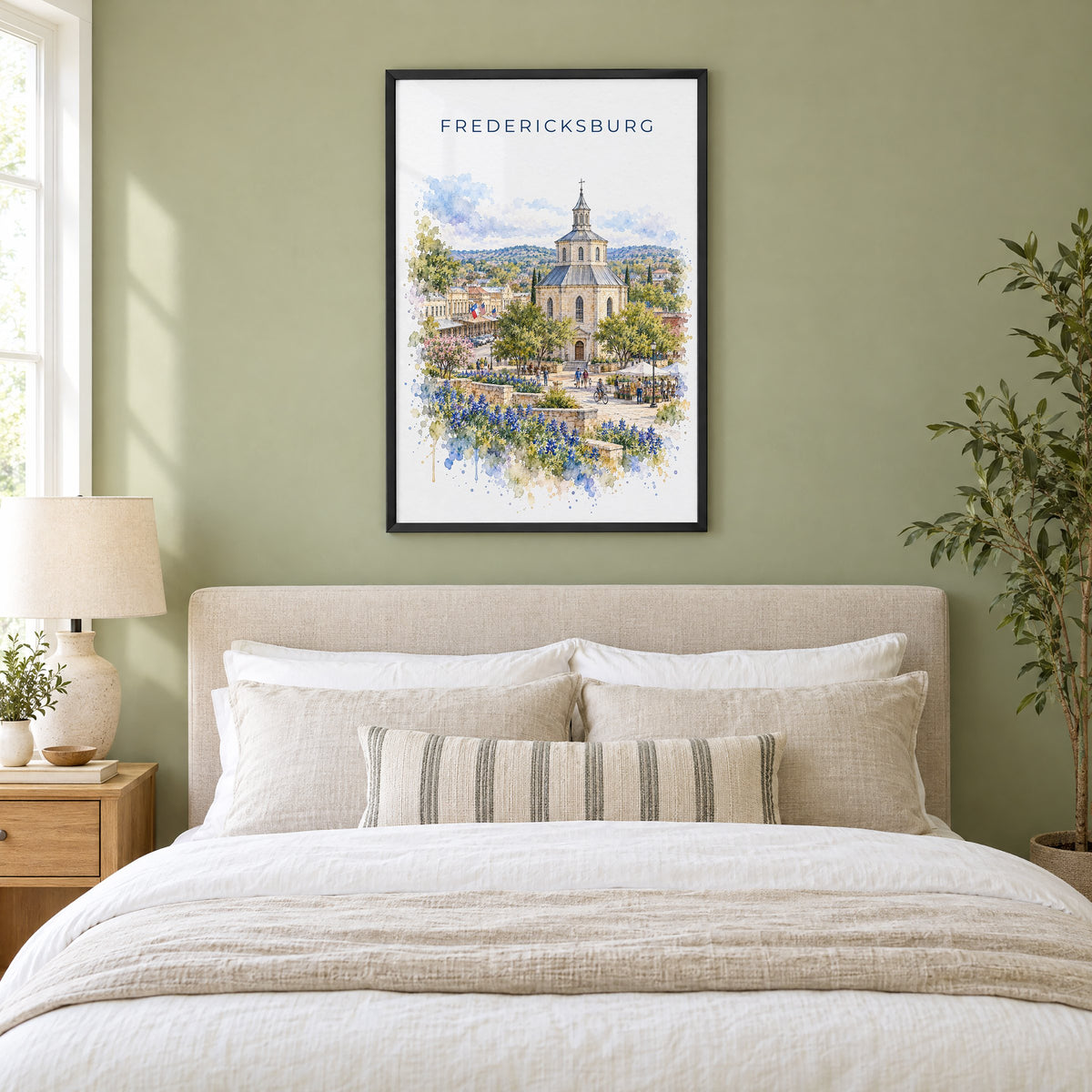 Fredericksburg, Texas watercolor print in a black frame above an upholstered headboard in a sage green bedroom