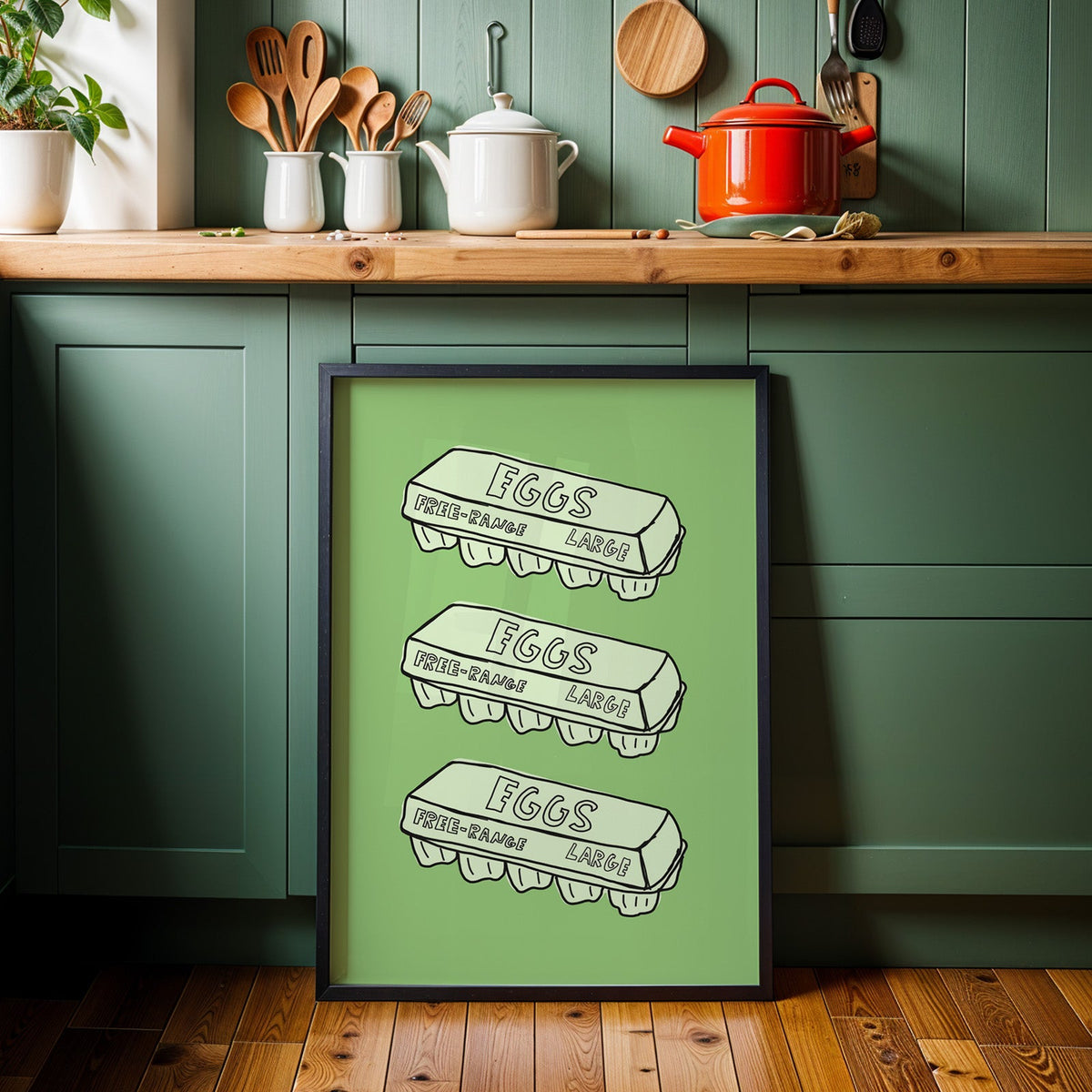 Free range eggs carton print in a black frame against sage green kitchen cabinets