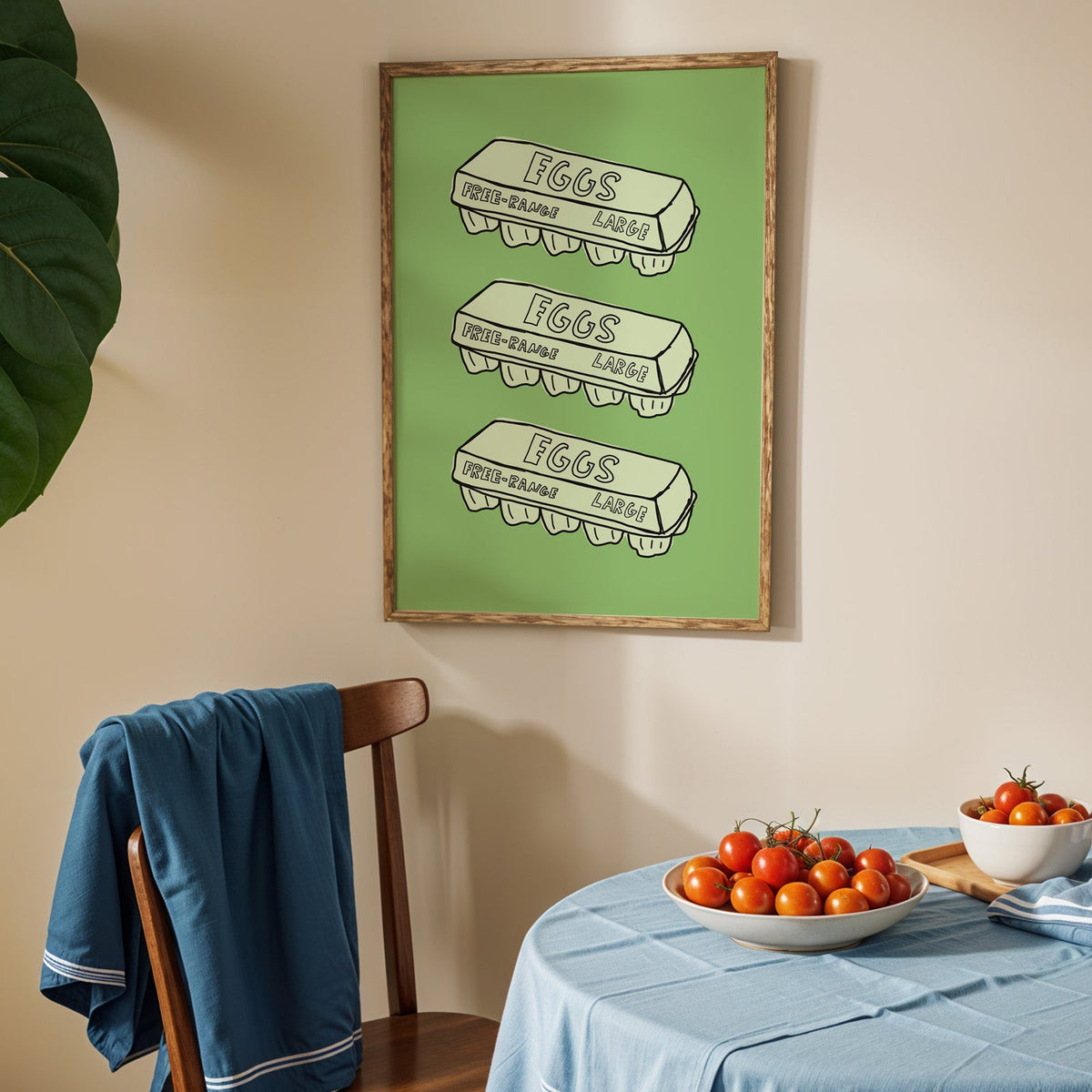Free range eggs carton print in an oak frame above a blue linen table with ripe tomatoes