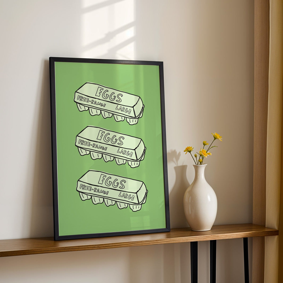 Free range eggs carton print in a black frame on a console table with yellow daisies
