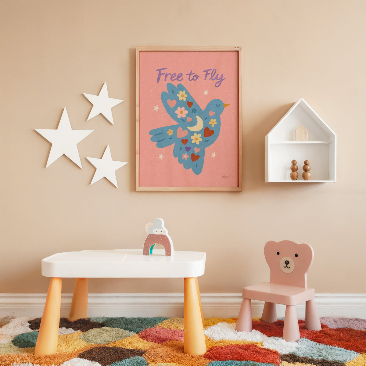 Folk blue bird free to fly nursery print in an oak frame on a peach wall above a kids table with wall stars